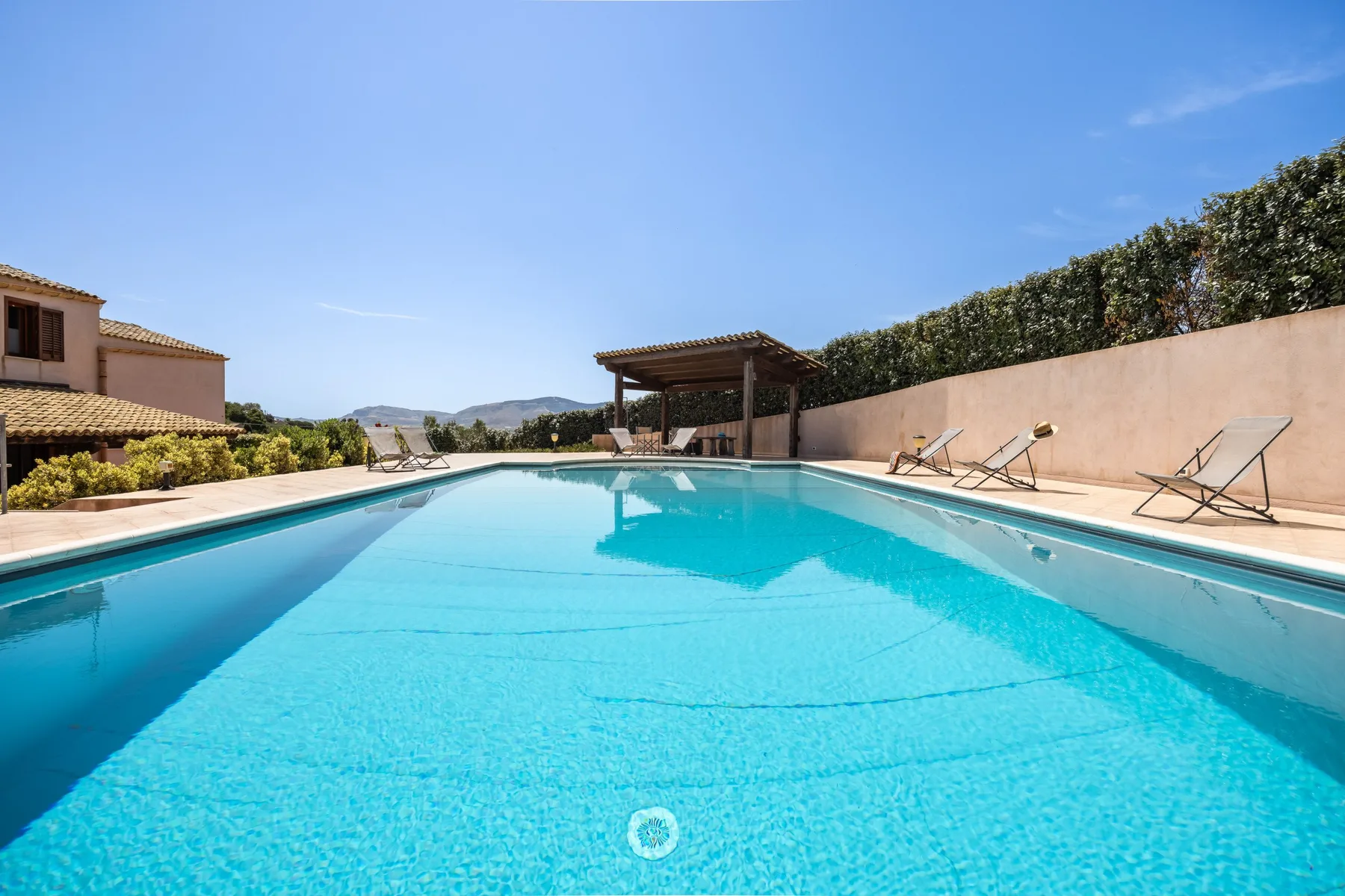 An outdoor swimming pool beside a patio with lounge chairs and a shaded pergola.