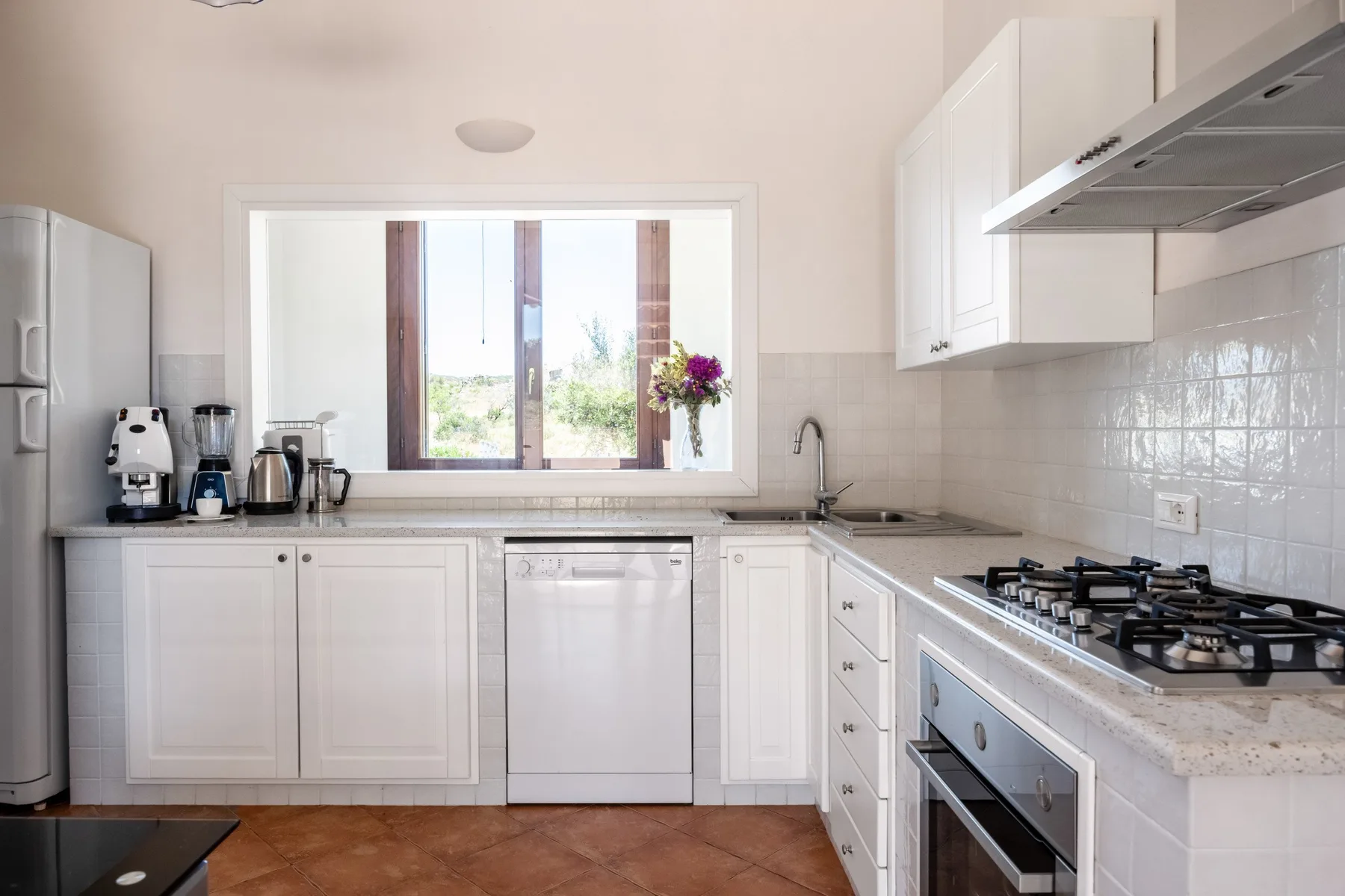 A bright kitchen with white cabinetry, a window, and countertop appliances.
