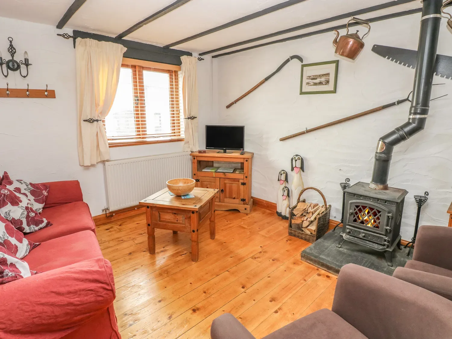Una sala de estar con un sofá rojo, una estufa de leña y muebles de madera en Cowslip Cottage, en Rosemarket.