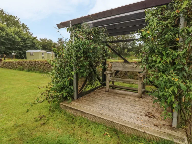 Una pérgola de jardín con un banco de madera está junto a un césped.