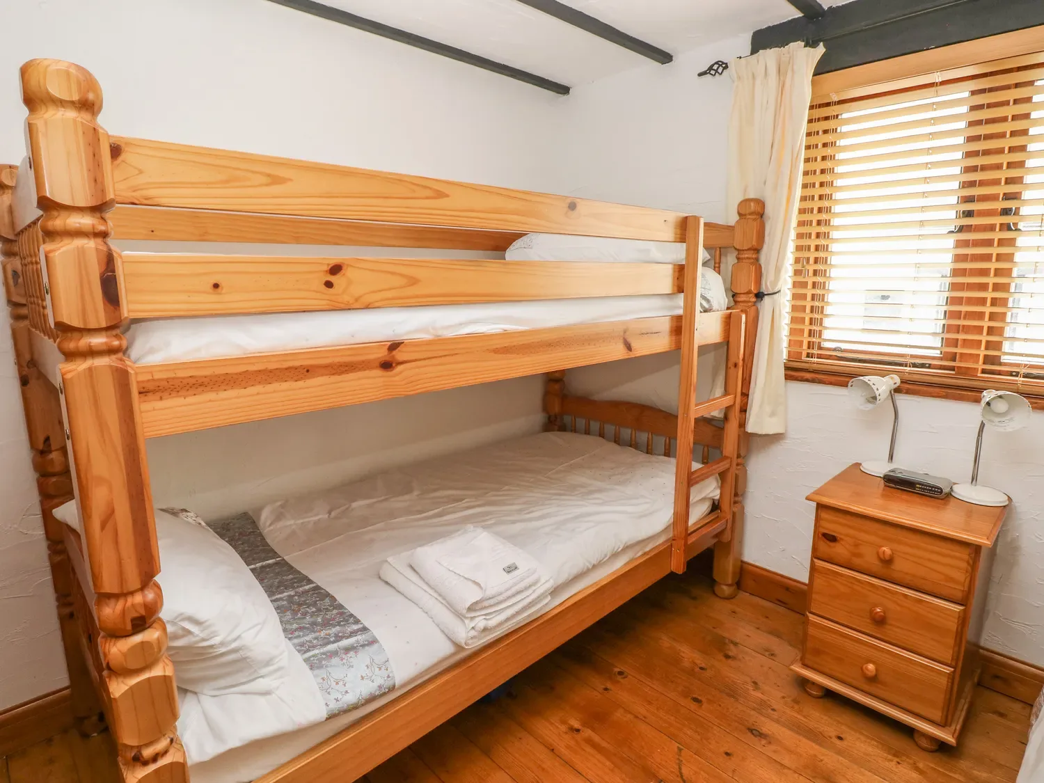 Un dormitorio con literas de madera junto a una ventana y una pequeña mesita de noche.