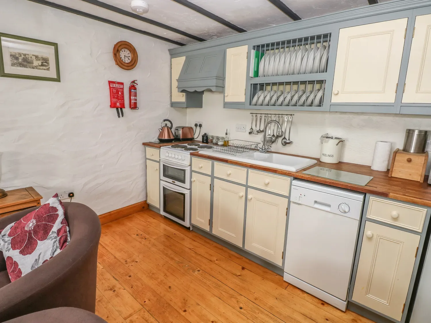 Una cocina con armarios de color crema y gris, cocina eléctrica, lavavajillas y fregadero en Cowslip Cottage, en Rosemarket.