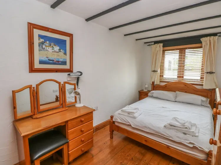 Un dormitorio con cama de madera, ropa de cama blanca y una cómoda junto a la ventana.