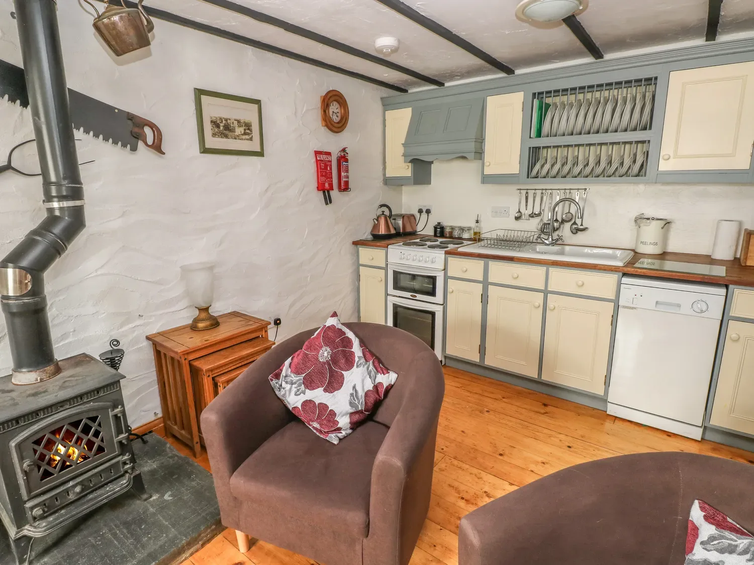 Una cocina con fregadero, cocina, lavavajillas y una estufa de leña junto a un sillón.