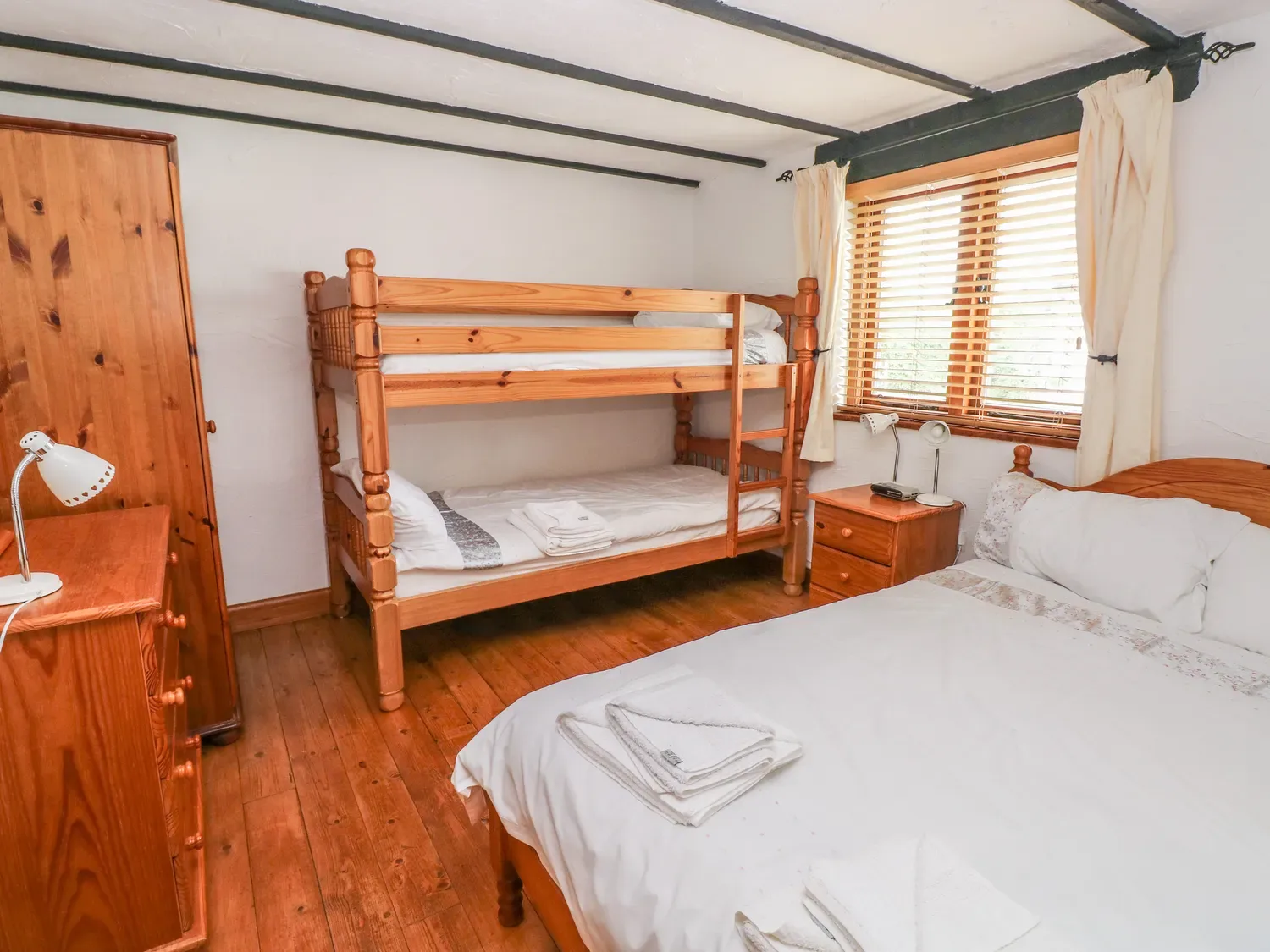 Un dormitorio con literas, una cama de matrimonio, muebles de madera y una ventana con estores en Cowslip Cottage, en Rosemarket.