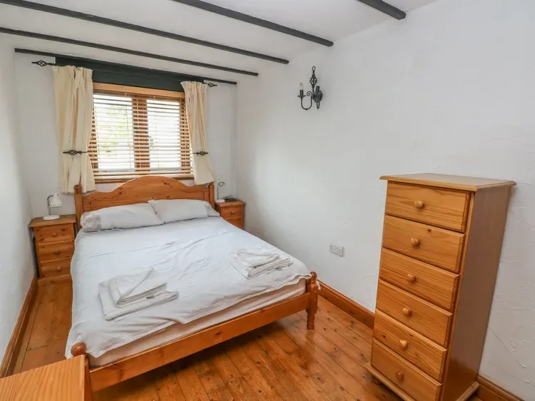 Un dormitorio con una cama de madera, ropa de cama blanca y una ventana con cortinas.