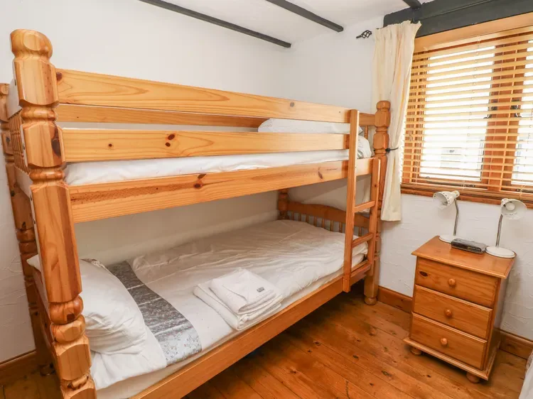 Una litera de madera ocupa un dormitorio compacto junto a una ventana con persianas.