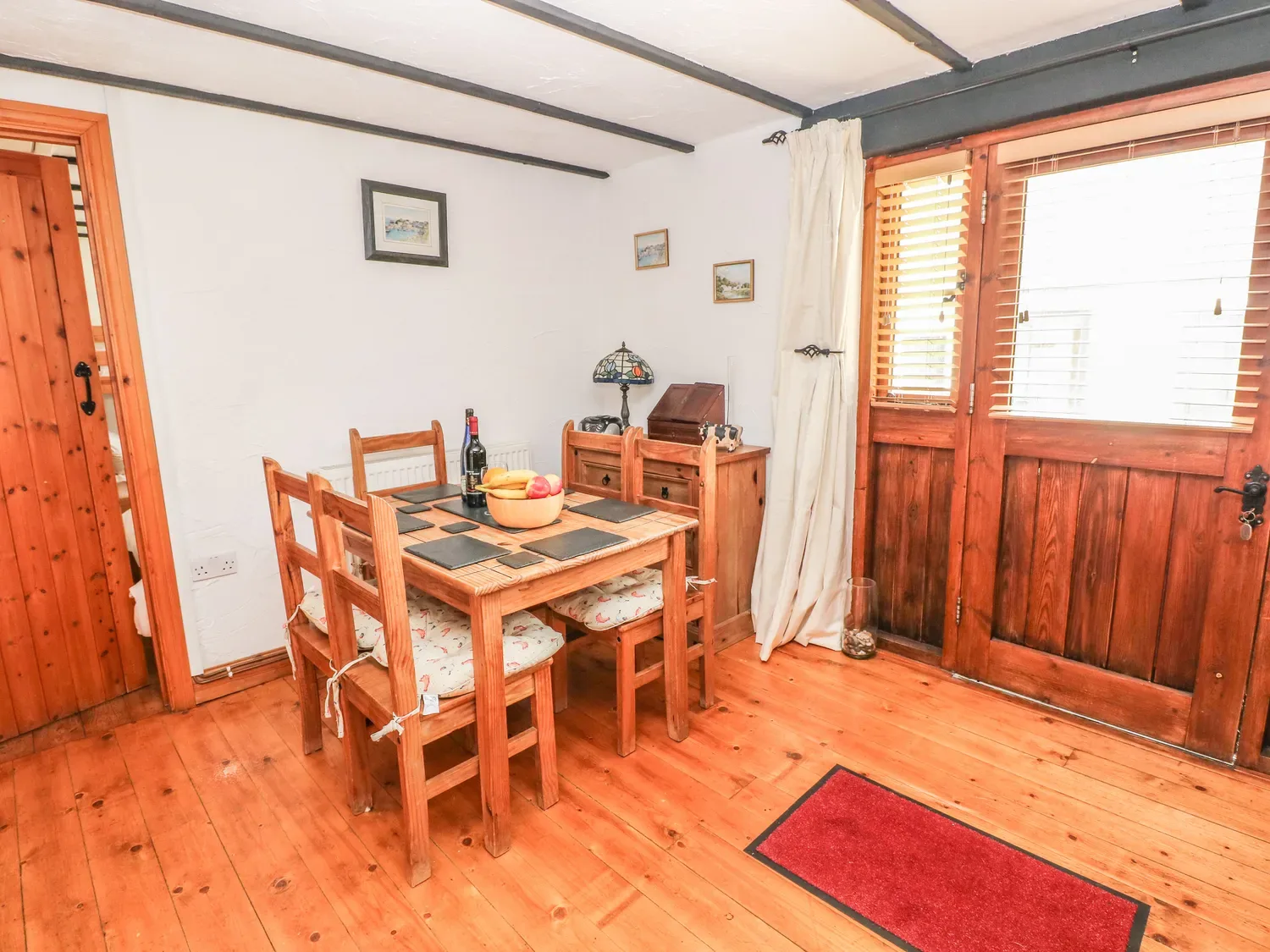 Una zona de comedor con mesa y sillas de madera junto a unas puertas de madera en Cowslip Cottage, en Rosemarket.