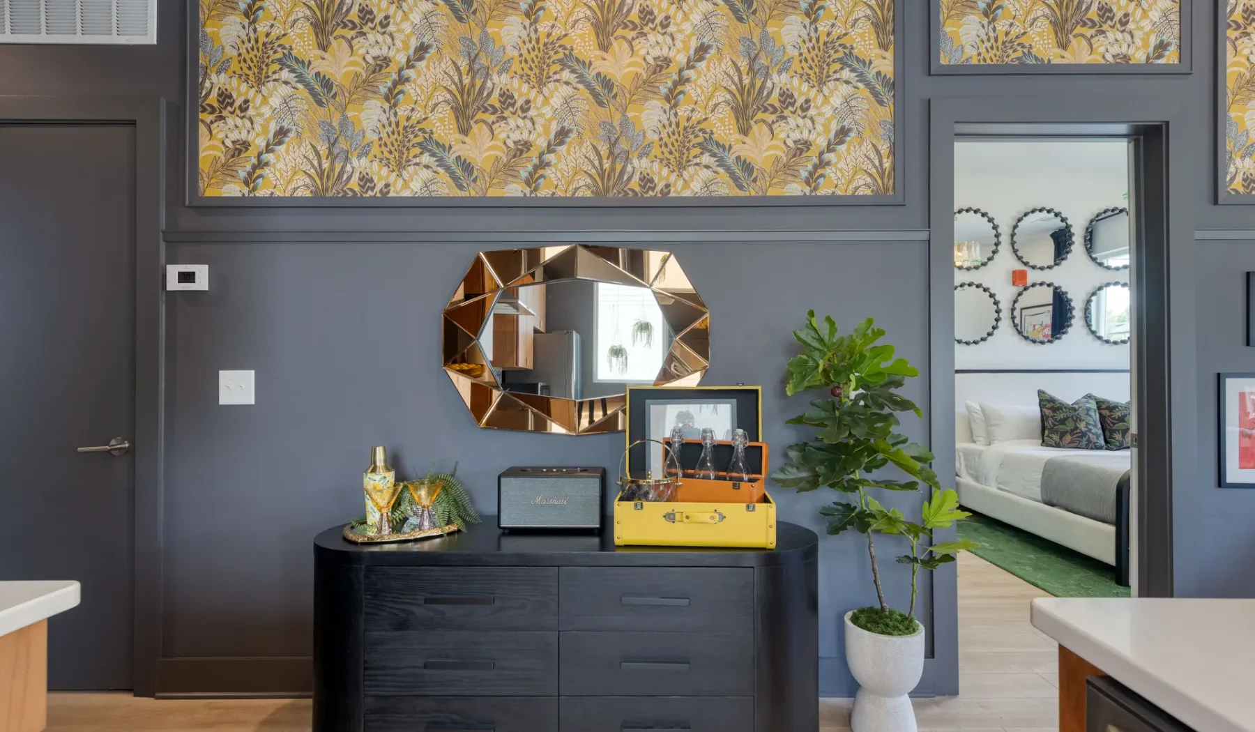 A dark-walled interior with a dresser, decorative mirror, and doorway to a seating area.