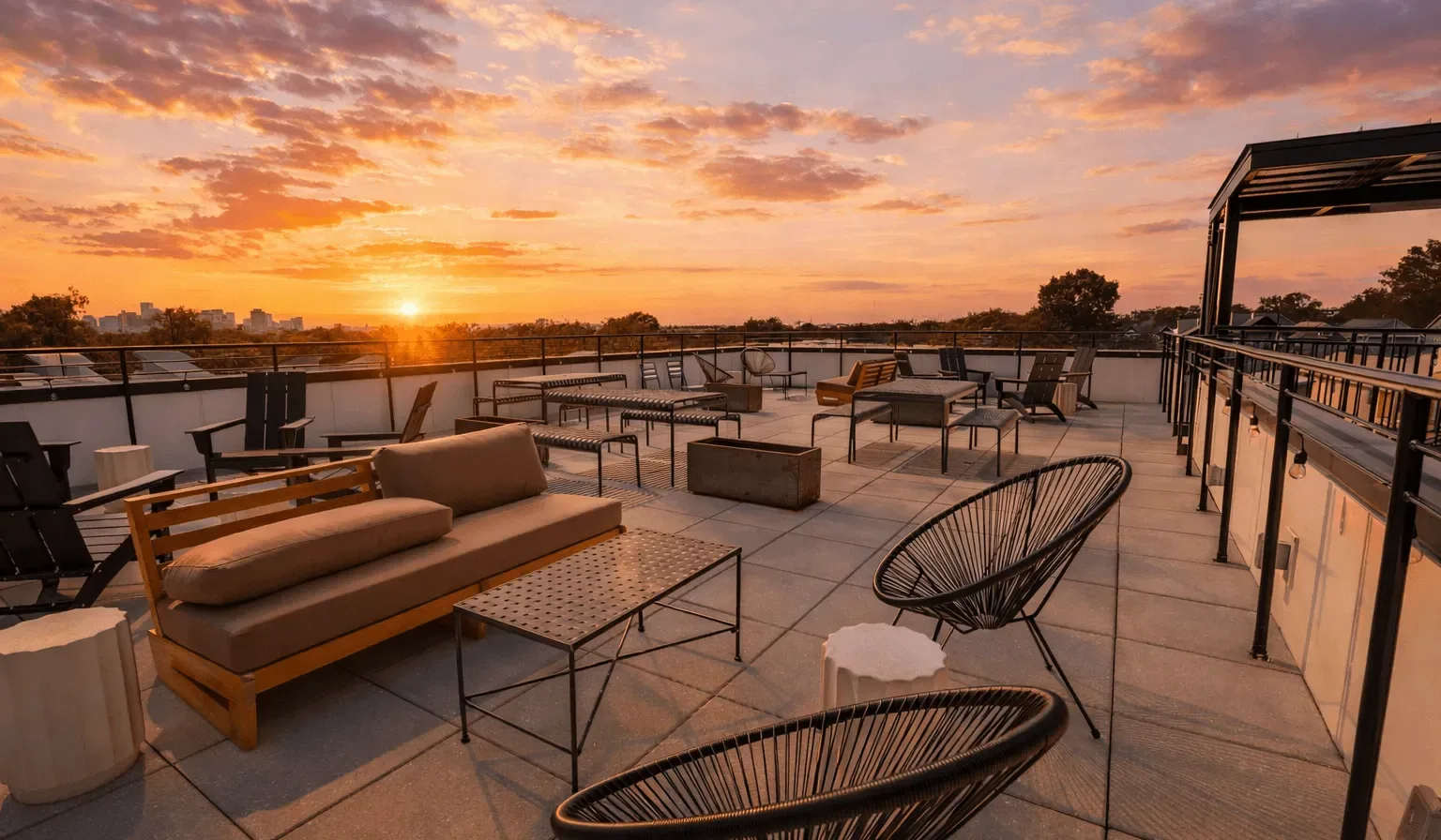 A rooftop terrace with outdoor seating overlooks the city at sunset.
