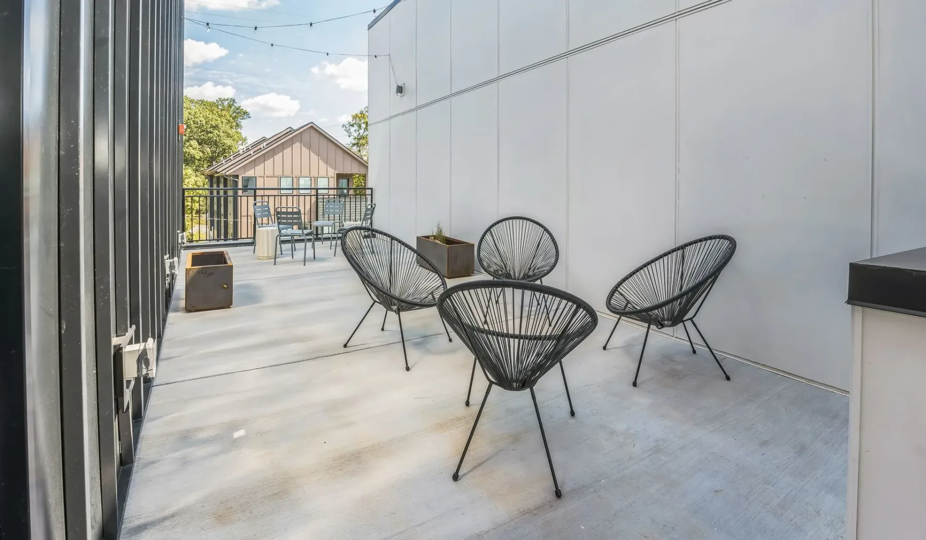An outdoor patio has wire seating beside a white wall.