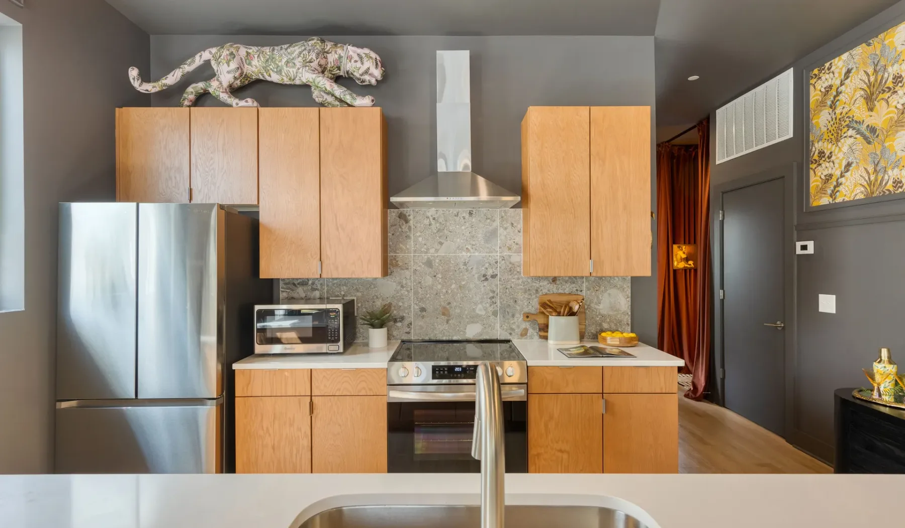 A modern kitchen with wooden cabinets, stainless steel appliances, and a stone backsplash.