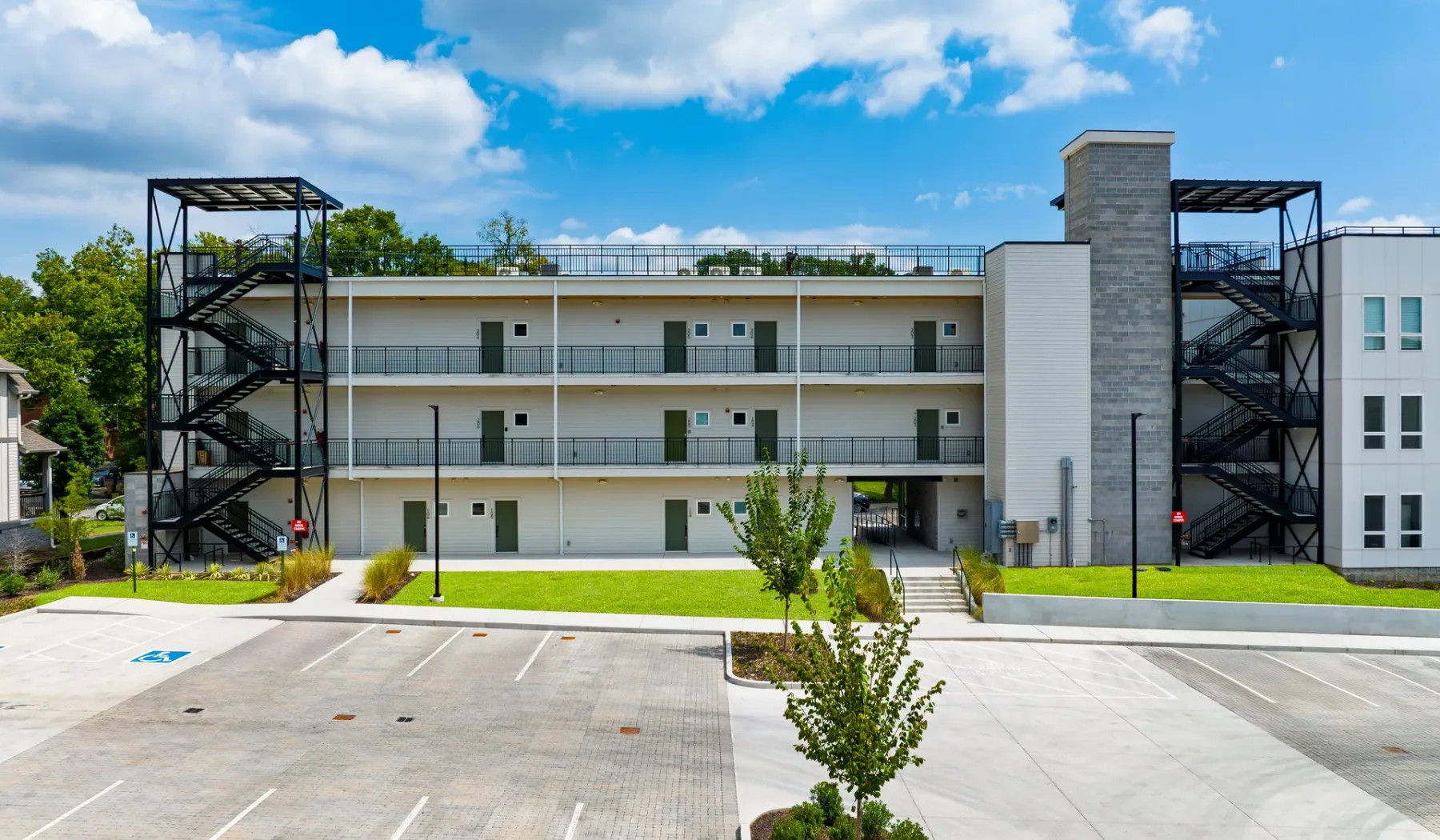 A multi-story apartment building with exterior walkways faces a paved parking area.