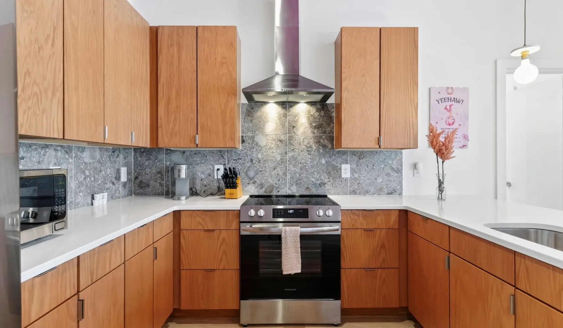 A modern kitchen with wooden cabinets, stone countertops, and a central range.