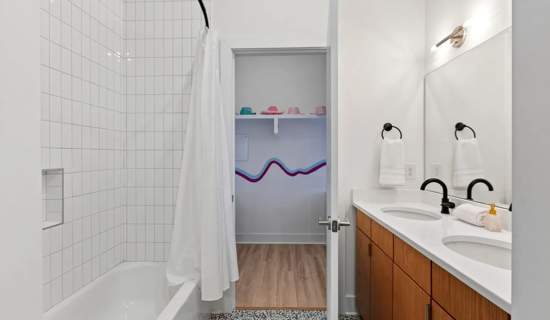 A bathroom with a tiled shower, double sinks, and an open doorway.