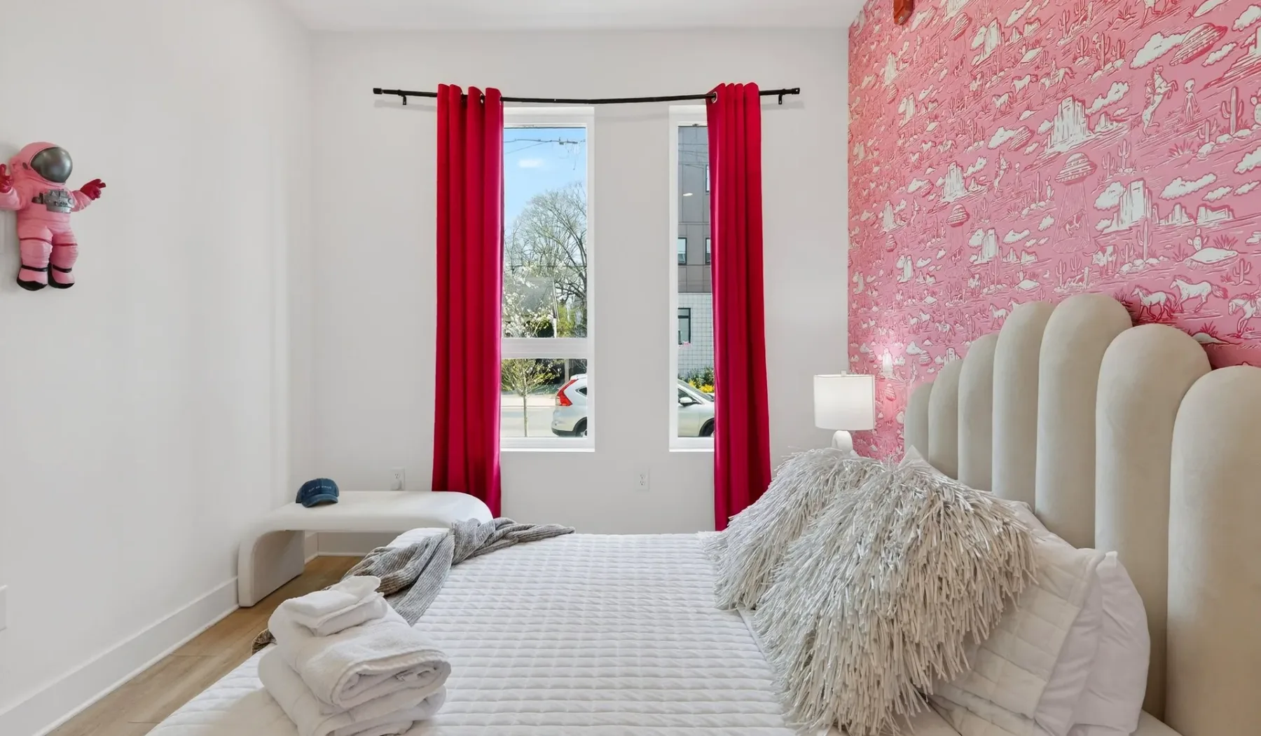 A bedroom with a white bed, red curtains, and a pink patterned wall.