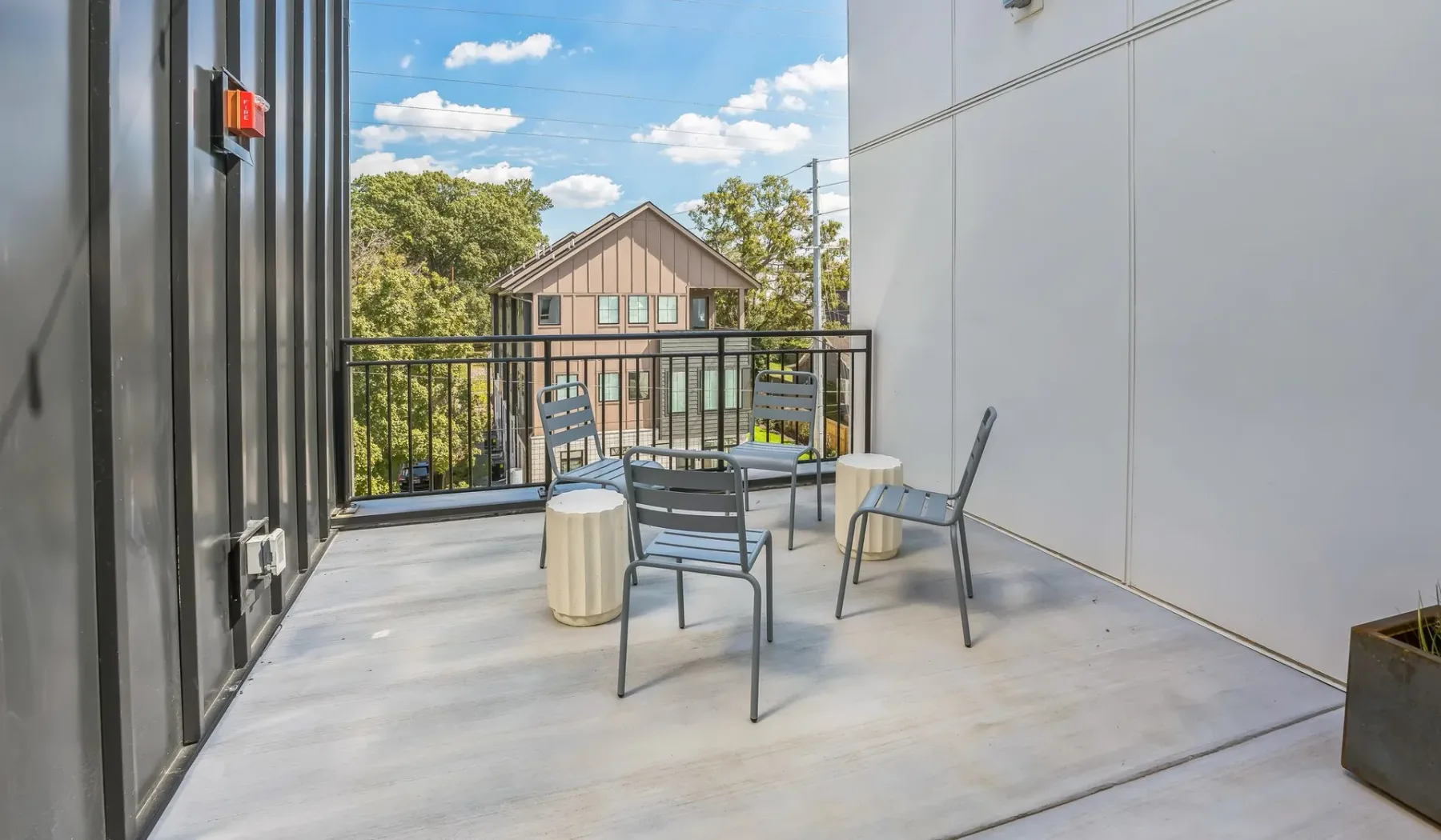 A rooftop patio has metal seating and a railing overlooking nearby buildings and trees.