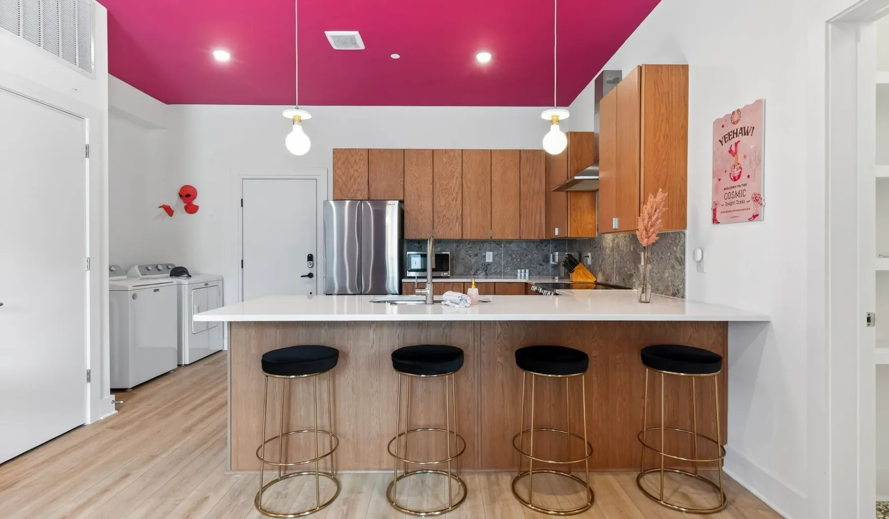 A kitchen with a large island and seating beneath a bright magenta ceiling.