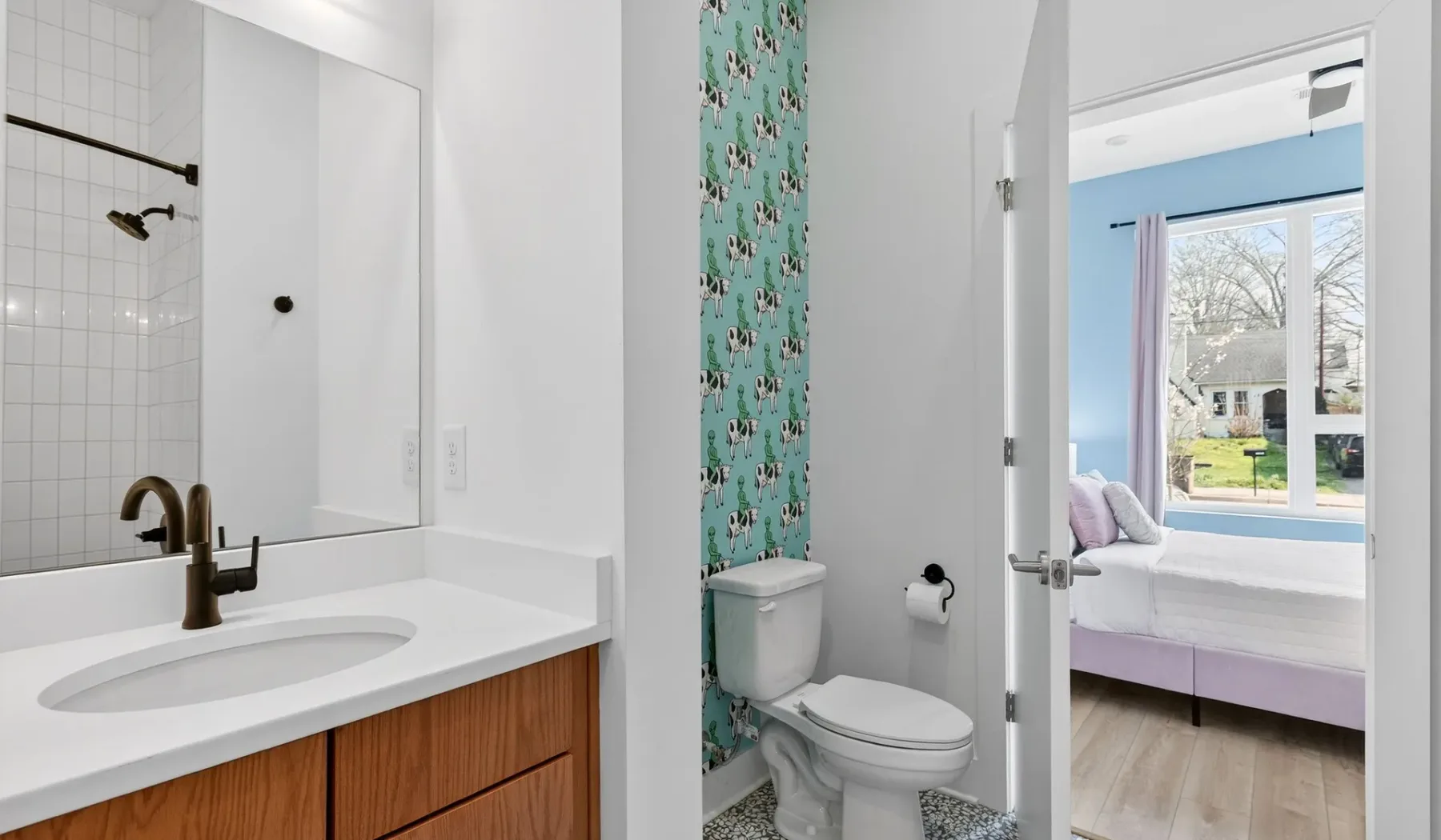 A bathroom vanity and toilet are visible beside an open doorway to a bedroom.