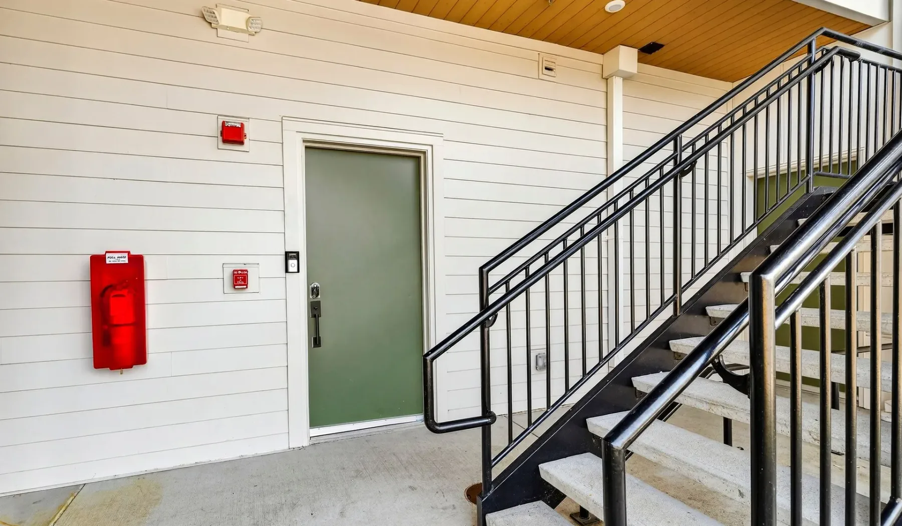 An indoor stairwell with a metal railing beside a green door.