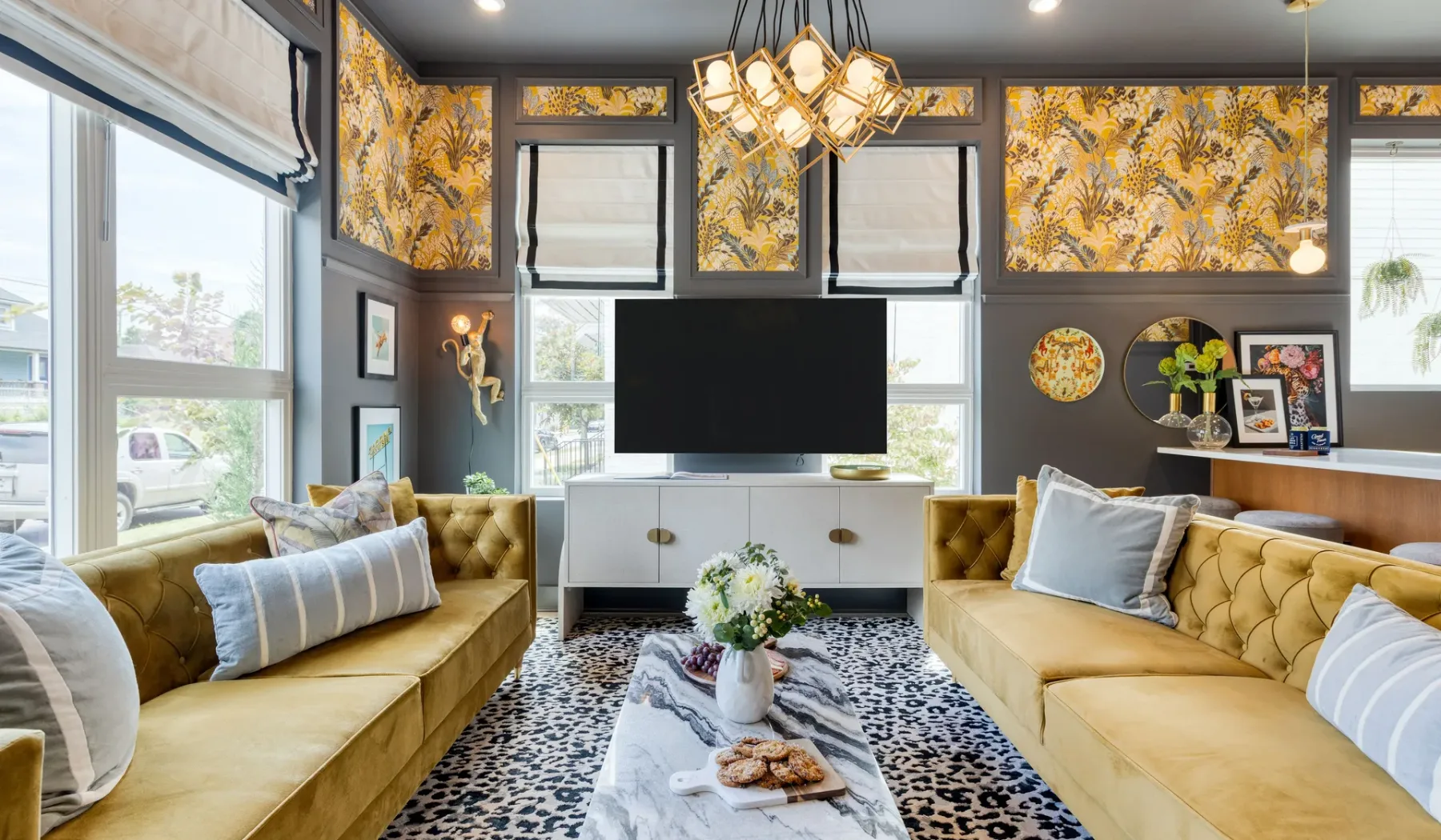 A living room with gold seating, a television, and large windows.