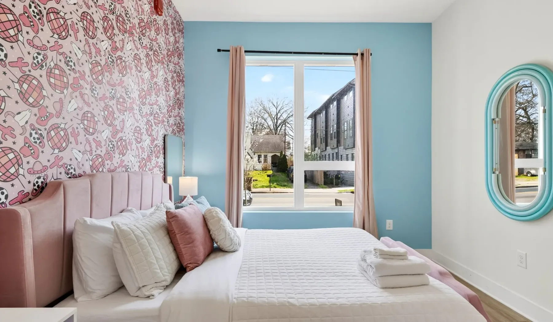 A bedroom with a bed, patterned wallpaper, and a window overlooking the street.