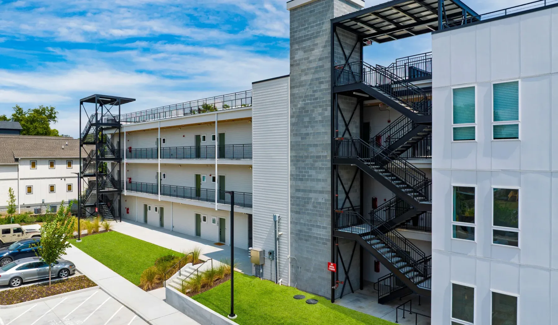A modern multi-story building with exterior staircases and parking nearby.