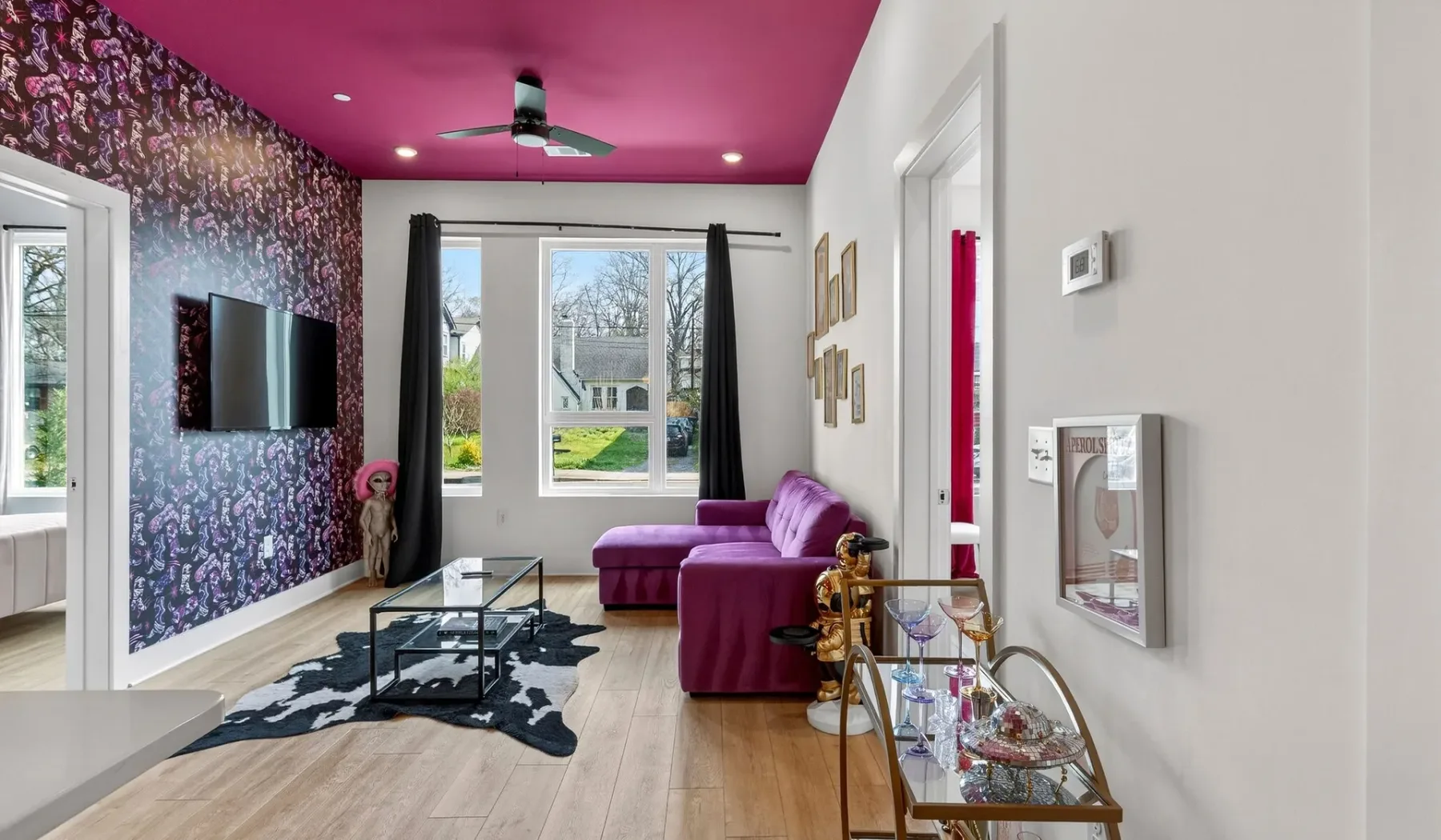 A colorful living room features purple seating, patterned walls, and large windows.