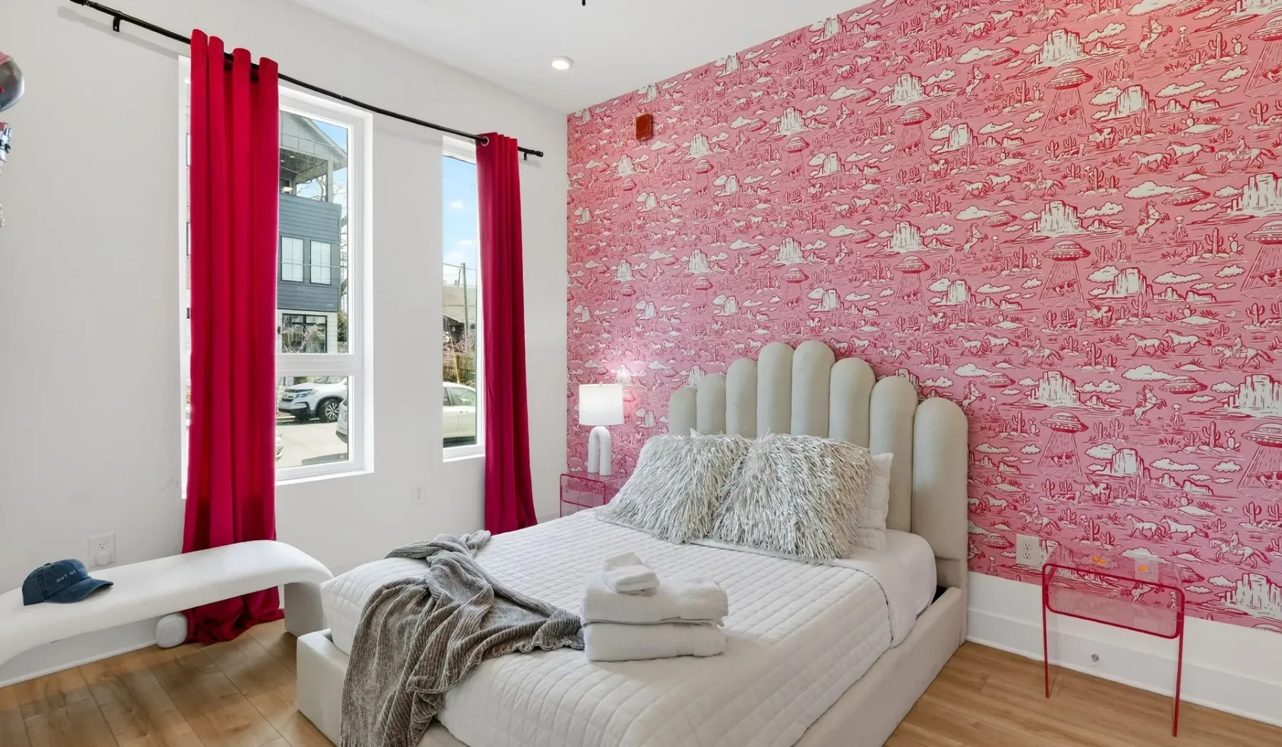 A bedroom with a bed, red curtains, and pink patterned wallpaper.