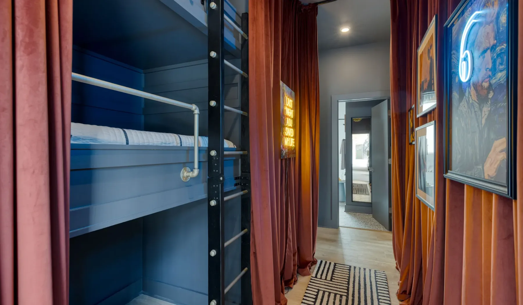 A narrow hallway with framed artwork and a bunk bed behind curtains.