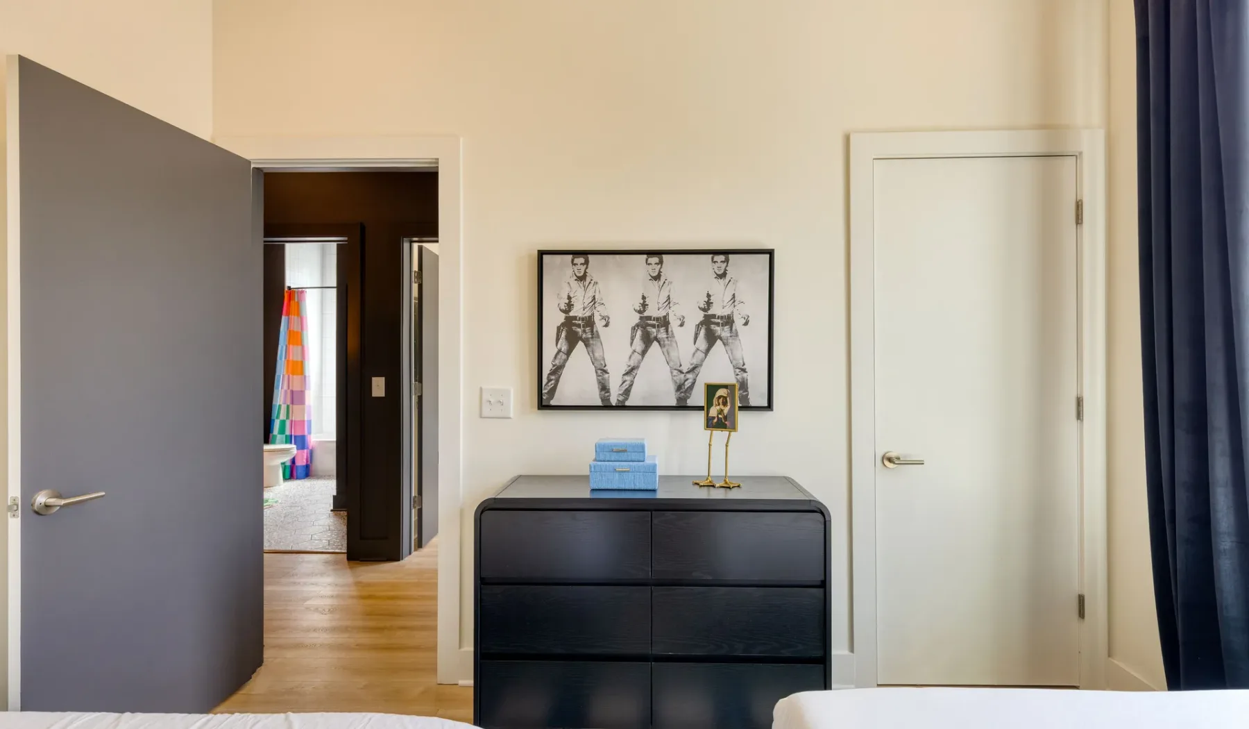 A bedroom doorway opens onto a wood-floored hall beside a black dresser.