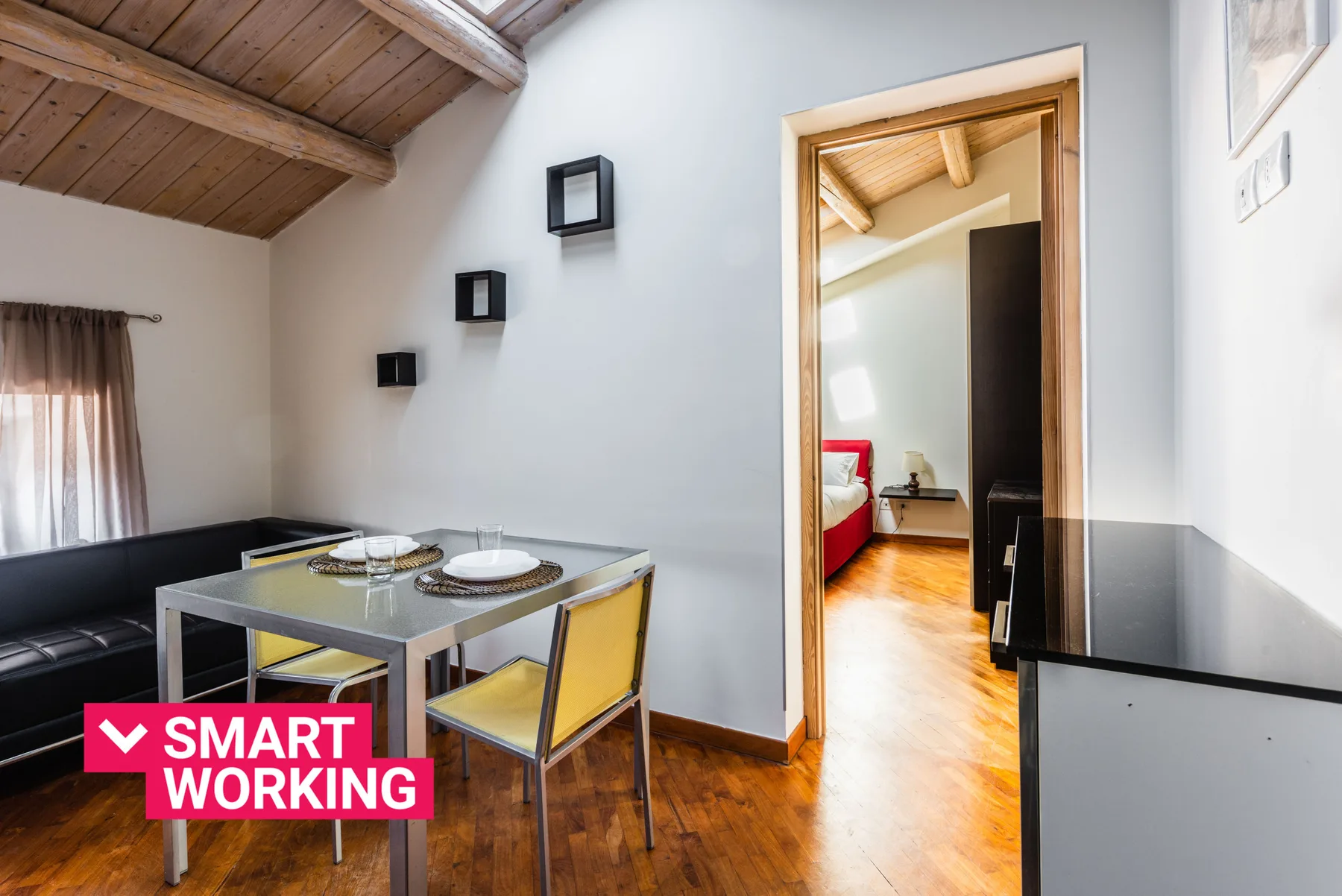 Comedor con la mesa puesta, asientos y una puerta abierta a un dormitorio.