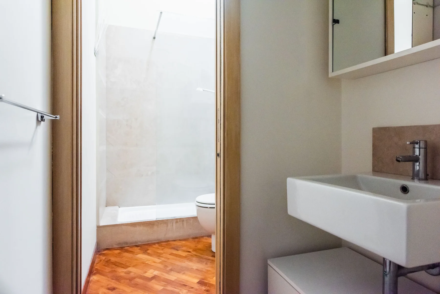 Un baño con un lavabo mural y una zona de ducha al otro lado de la puerta.