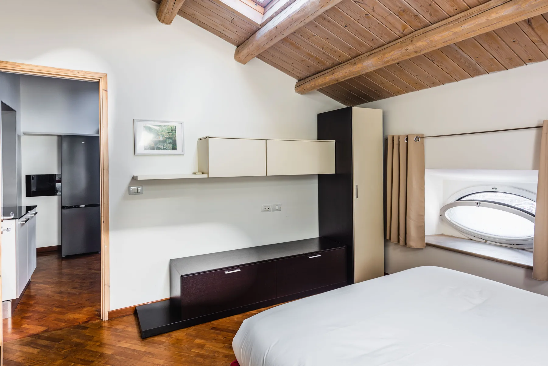 Un dormitorio con cama, televisor en la pared y vigas de madera a la vista.