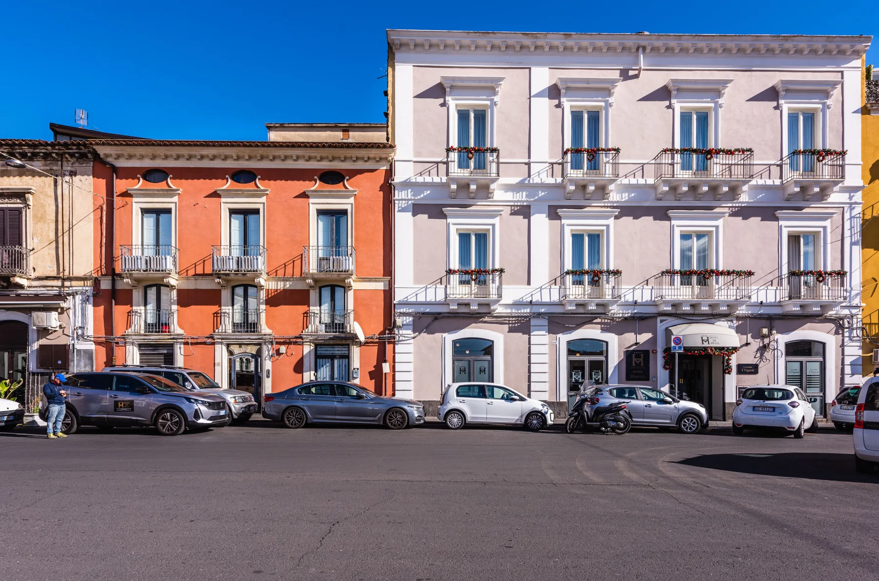 Una hilera de edificios coloridos de varias plantas con balcones da a una calle con vehículos estacionados.