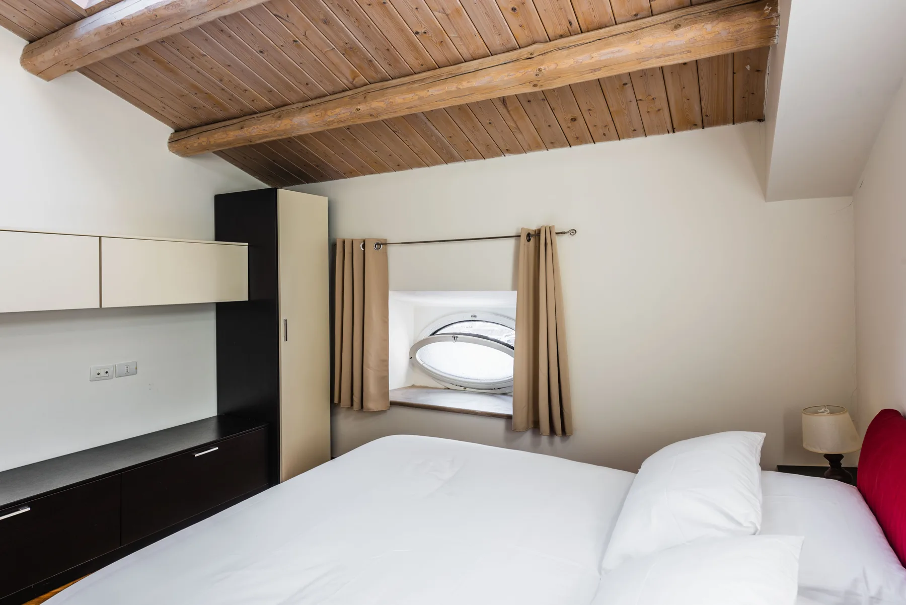 Un dormitorio con una cama bajo un techo inclinado de madera y una ventana pequeña.