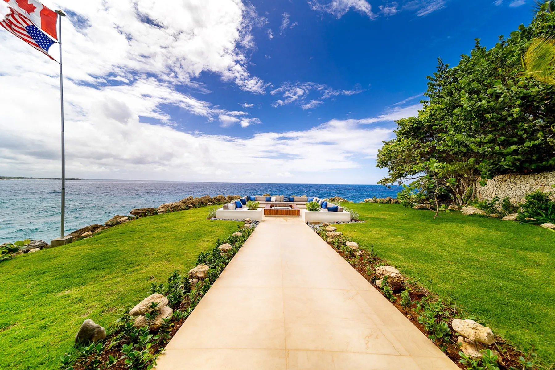 A seaside lawn with a paved path leading to a seating area by the water.