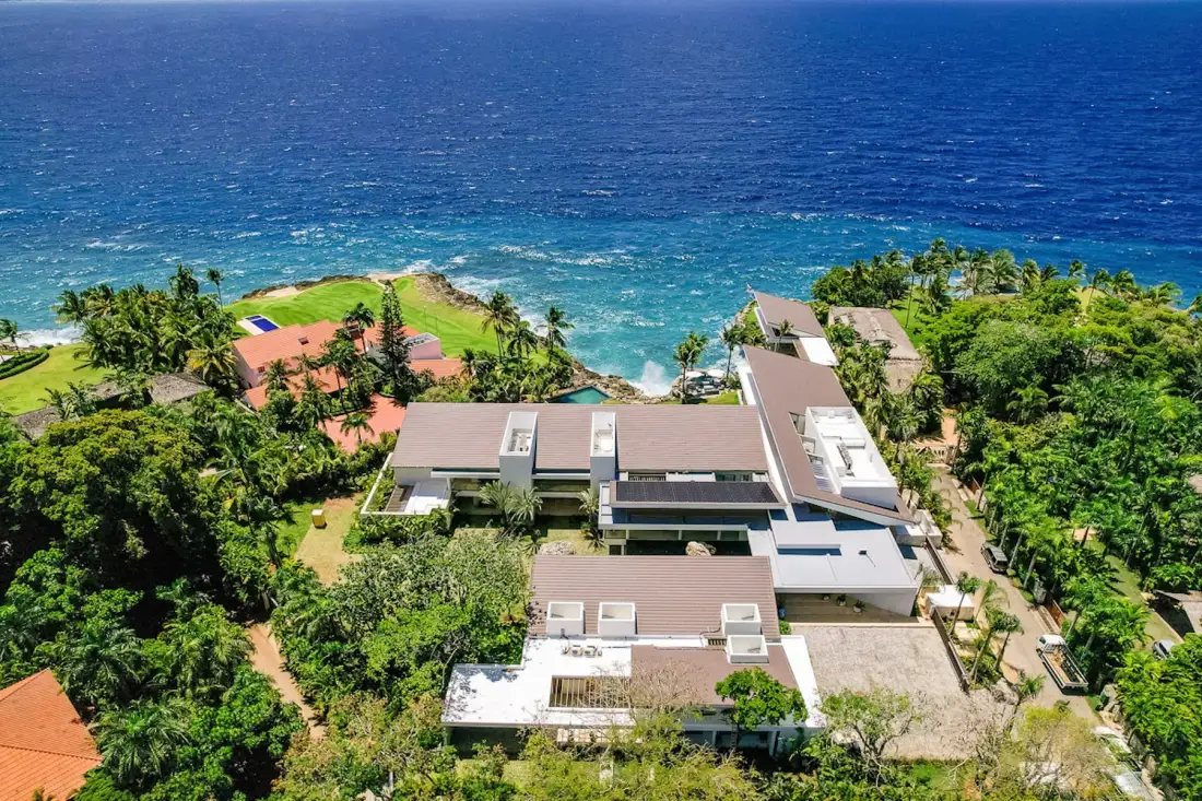 Aerial view of coastal buildings surrounded by greenery beside the ocean.