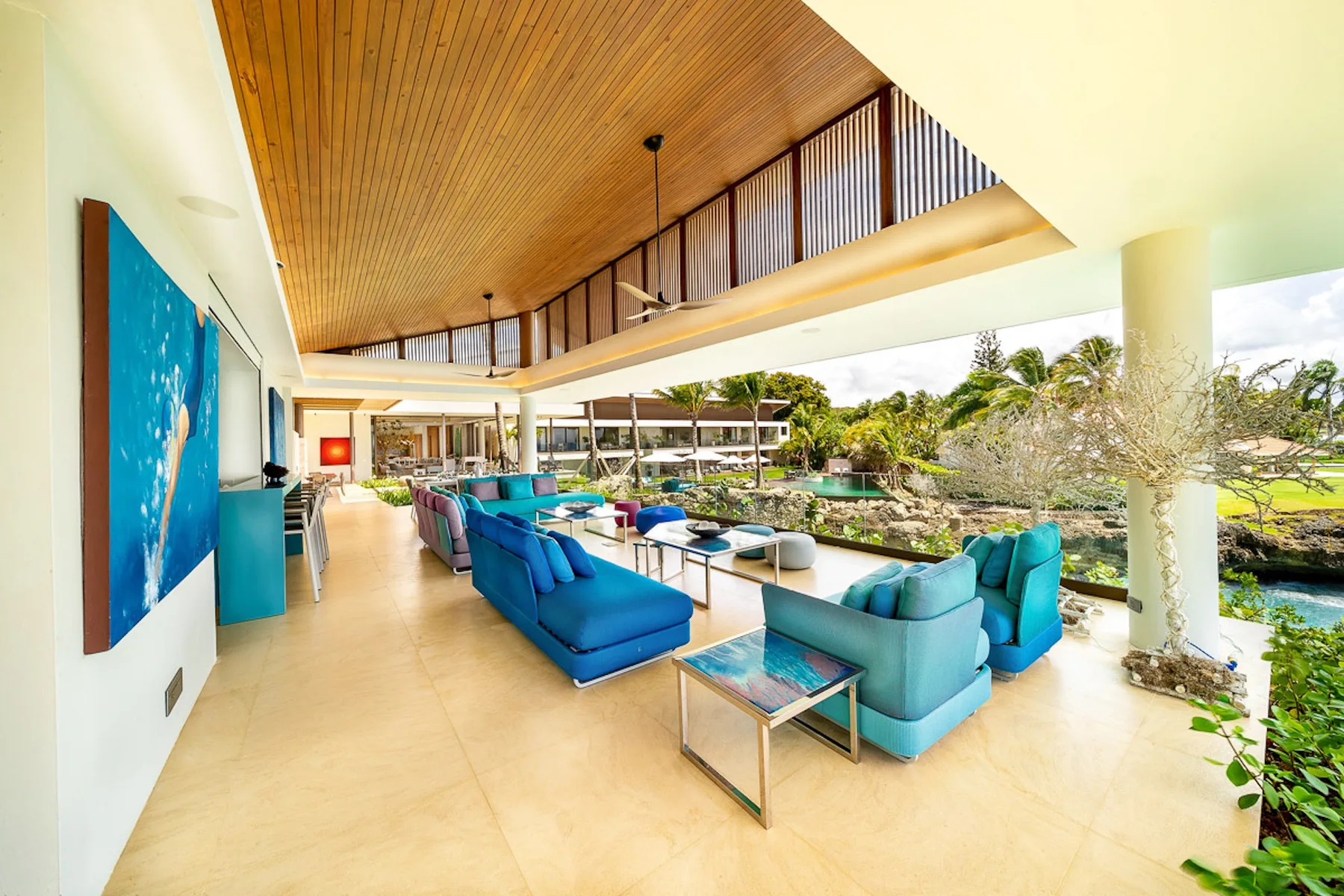 An open-air lounge with blue seating and a view of the pool and gardens.