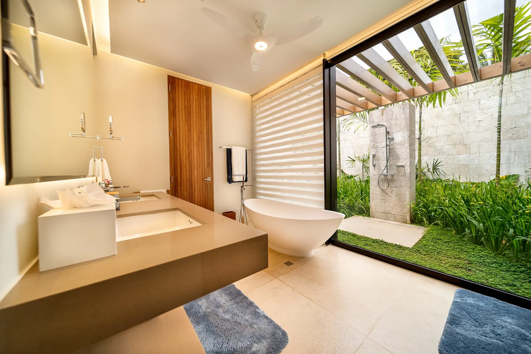 A bathroom with a bathtub, vanity, and an open view of a planted courtyard.