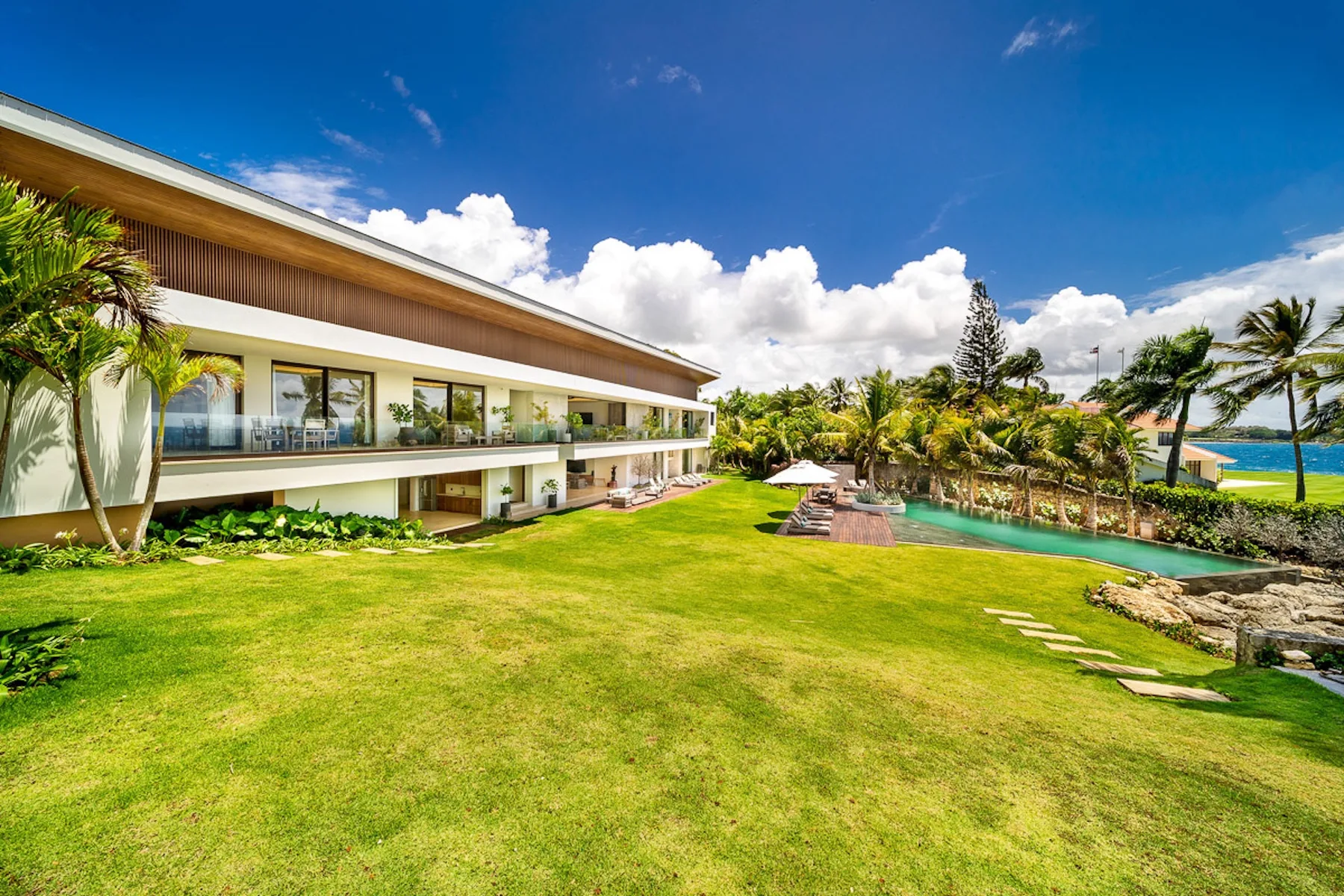A modern building overlooks a landscaped lawn, swimming pool, and ocean.