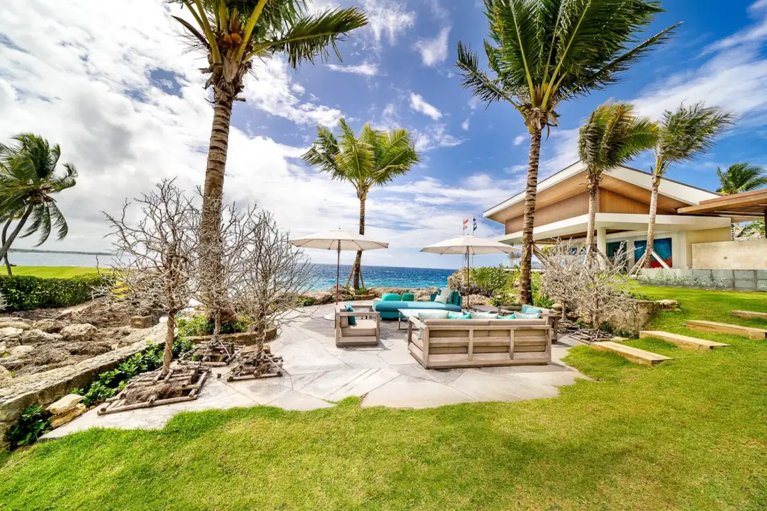 A seaside patio with outdoor seating, umbrellas, and palm trees.
