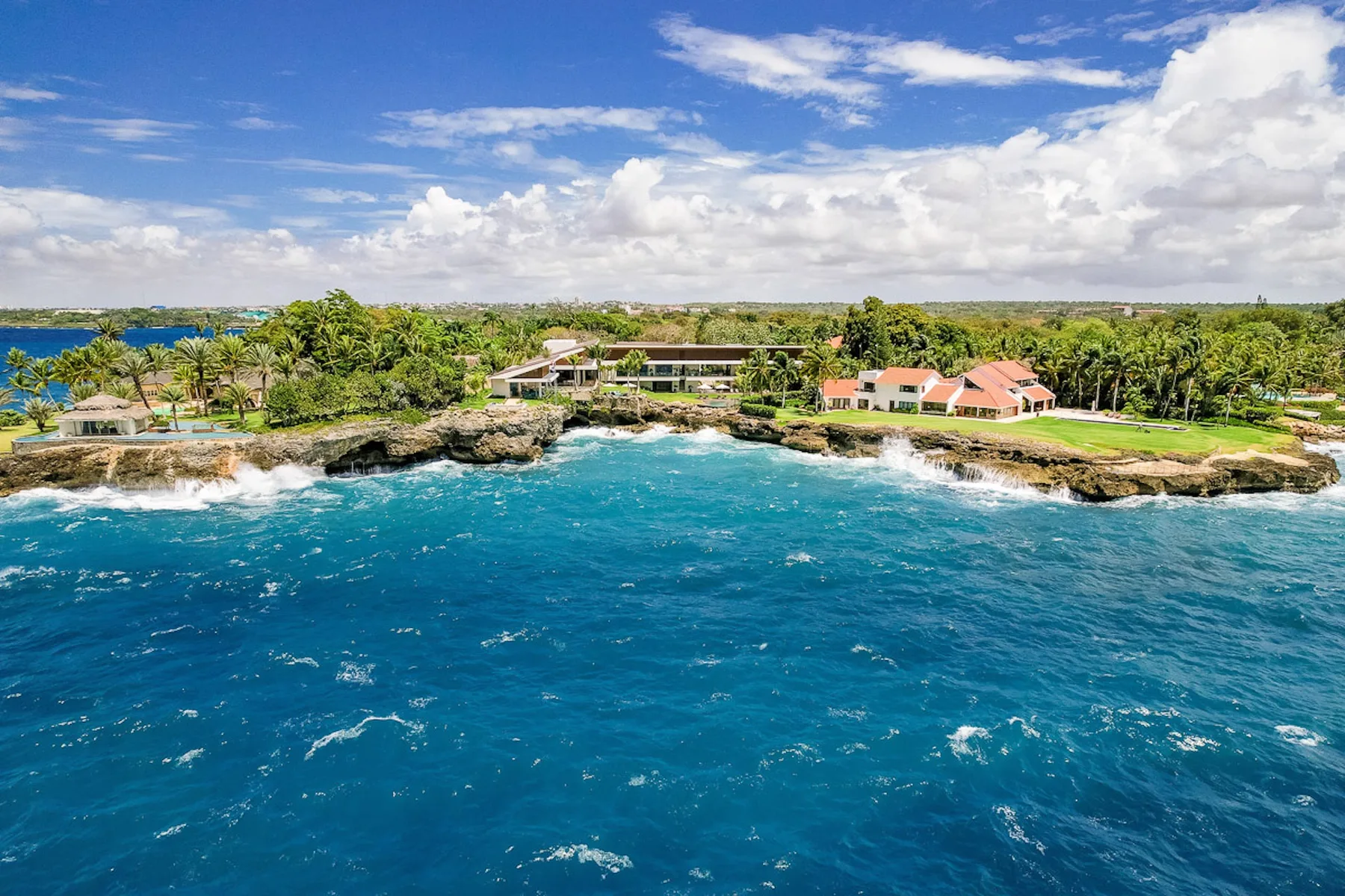 Coastal resort buildings sit among palm trees beside a turquoise ocean.