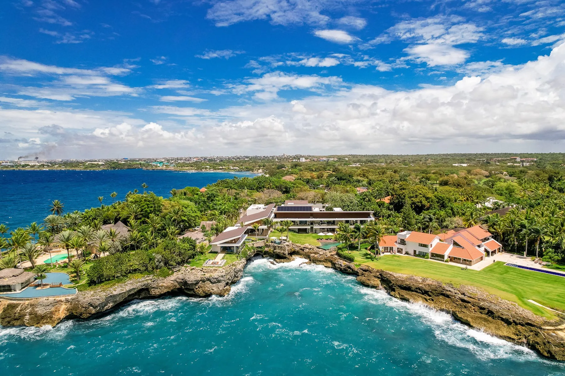 Aerial view of a coastal resort complex beside turquoise water and green grounds.