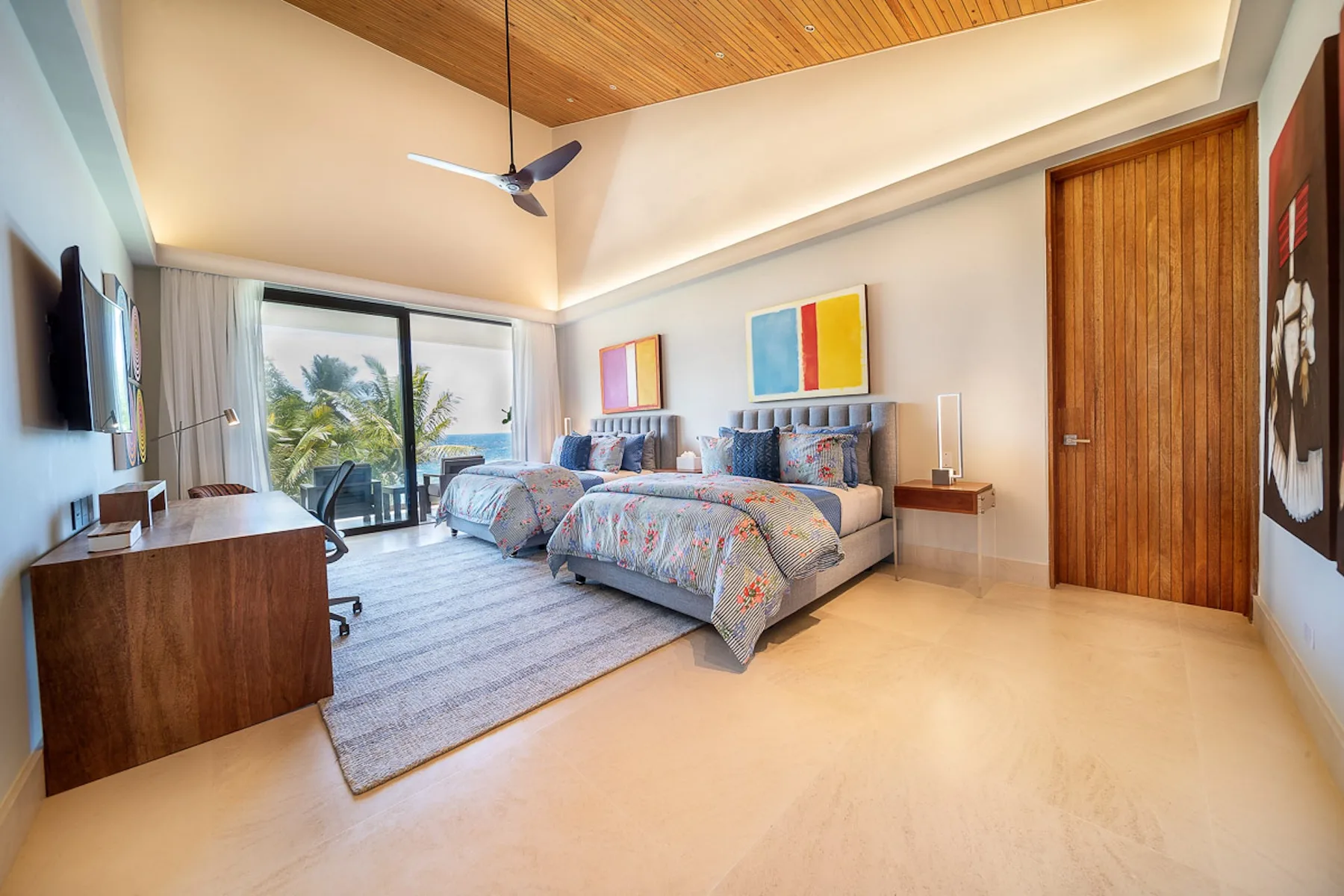 A bright bedroom with two beds, colorful artwork, and a sliding glass door.