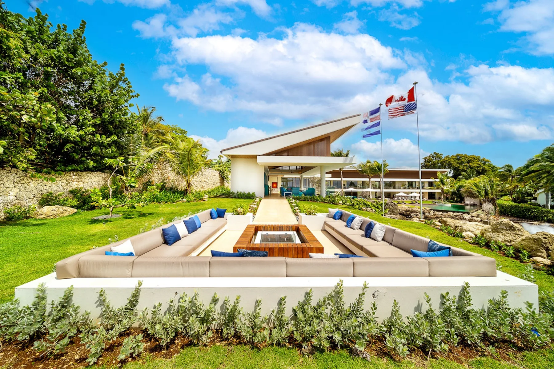 An outdoor lounge area with cushioned seating faces a modern building and flagpoles.