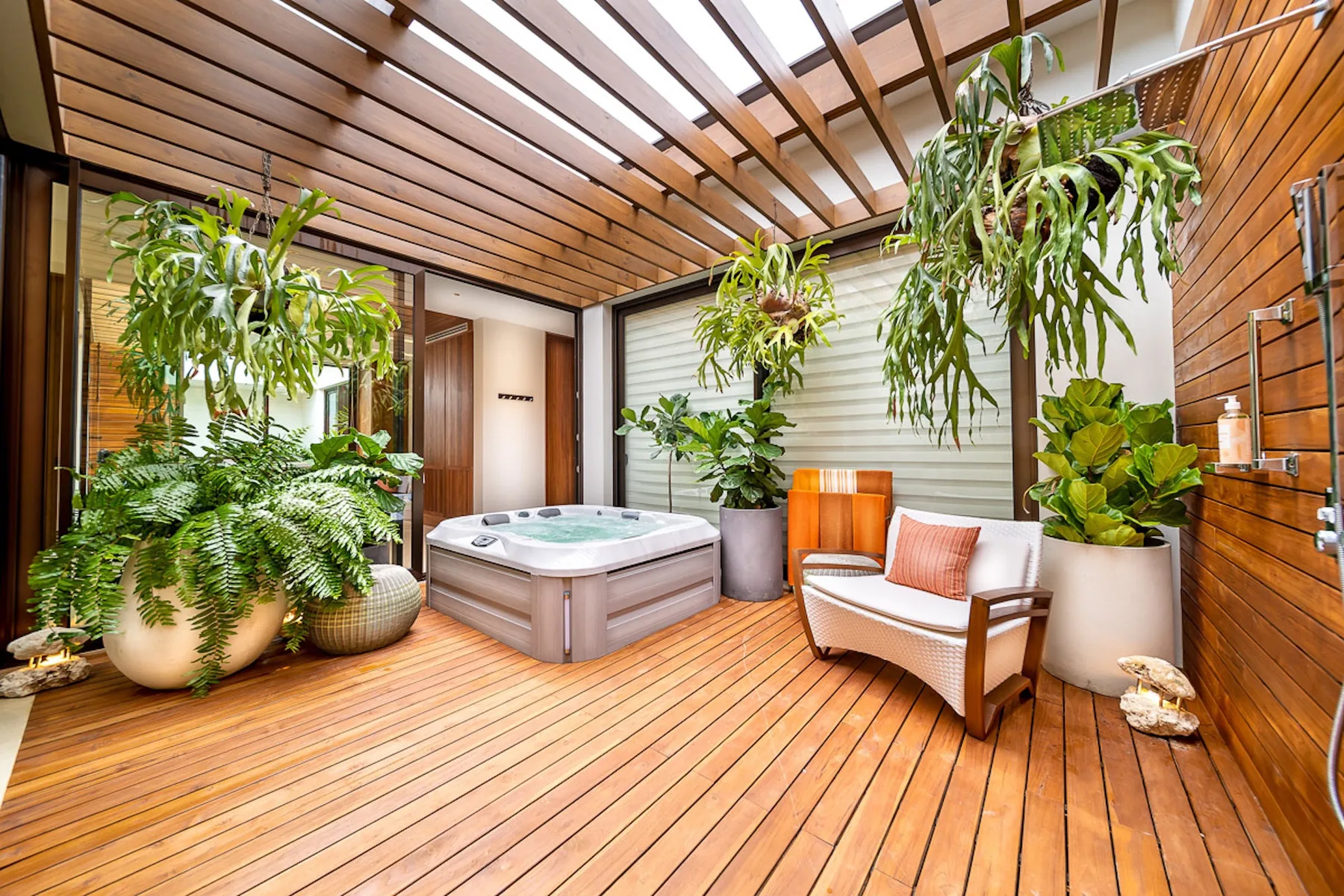 A covered patio with a hot tub, seating, and leafy plants.