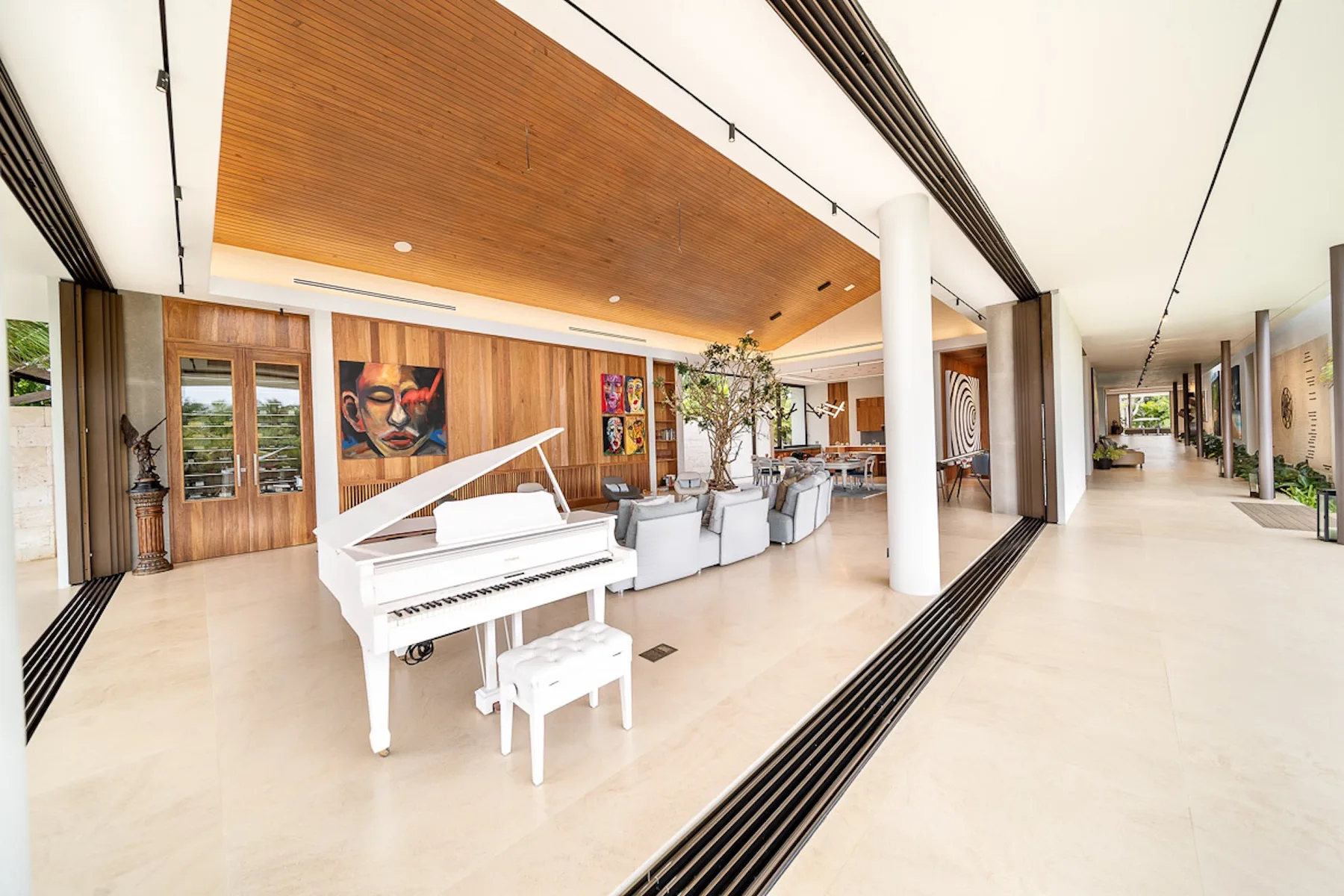 A spacious open lounge features a white grand piano and seating beneath a wood-paneled ceiling.