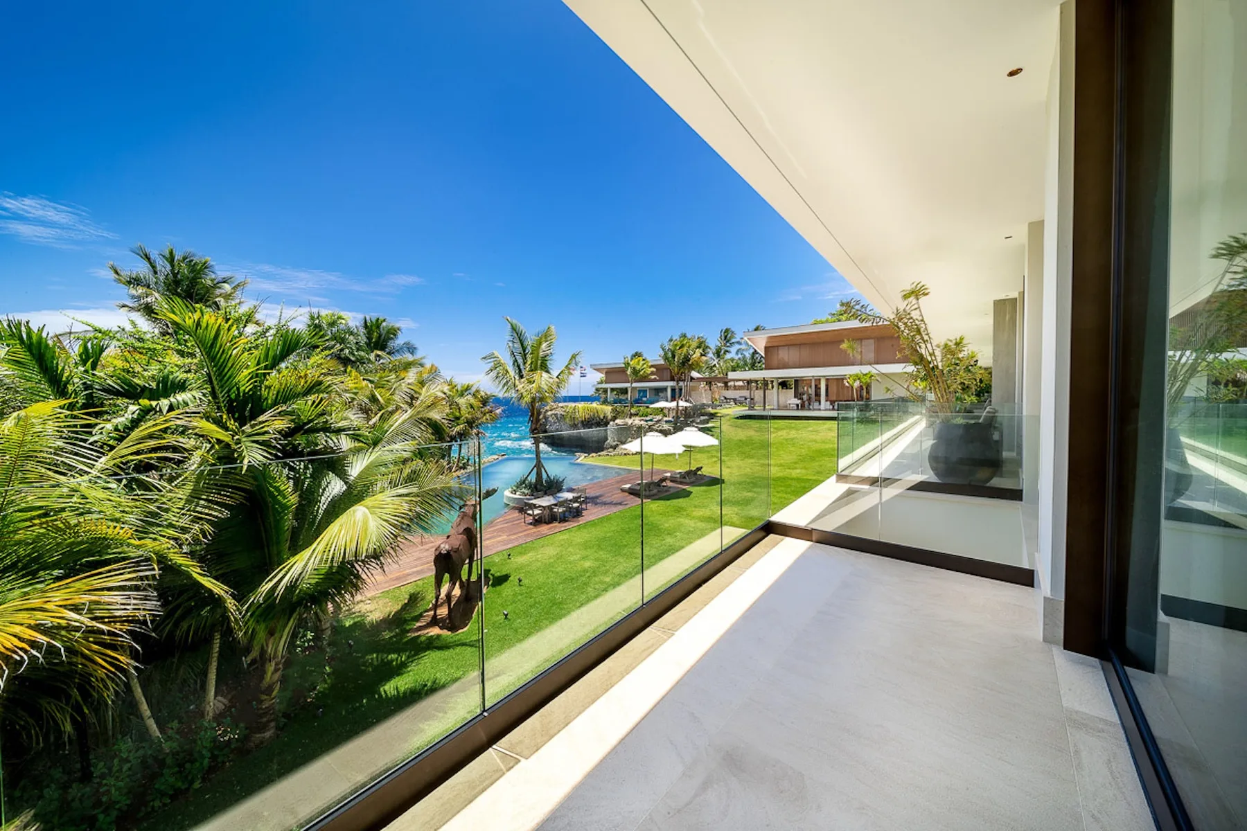 A bright balcony overlooks palm trees, landscaped grounds, and a pool.