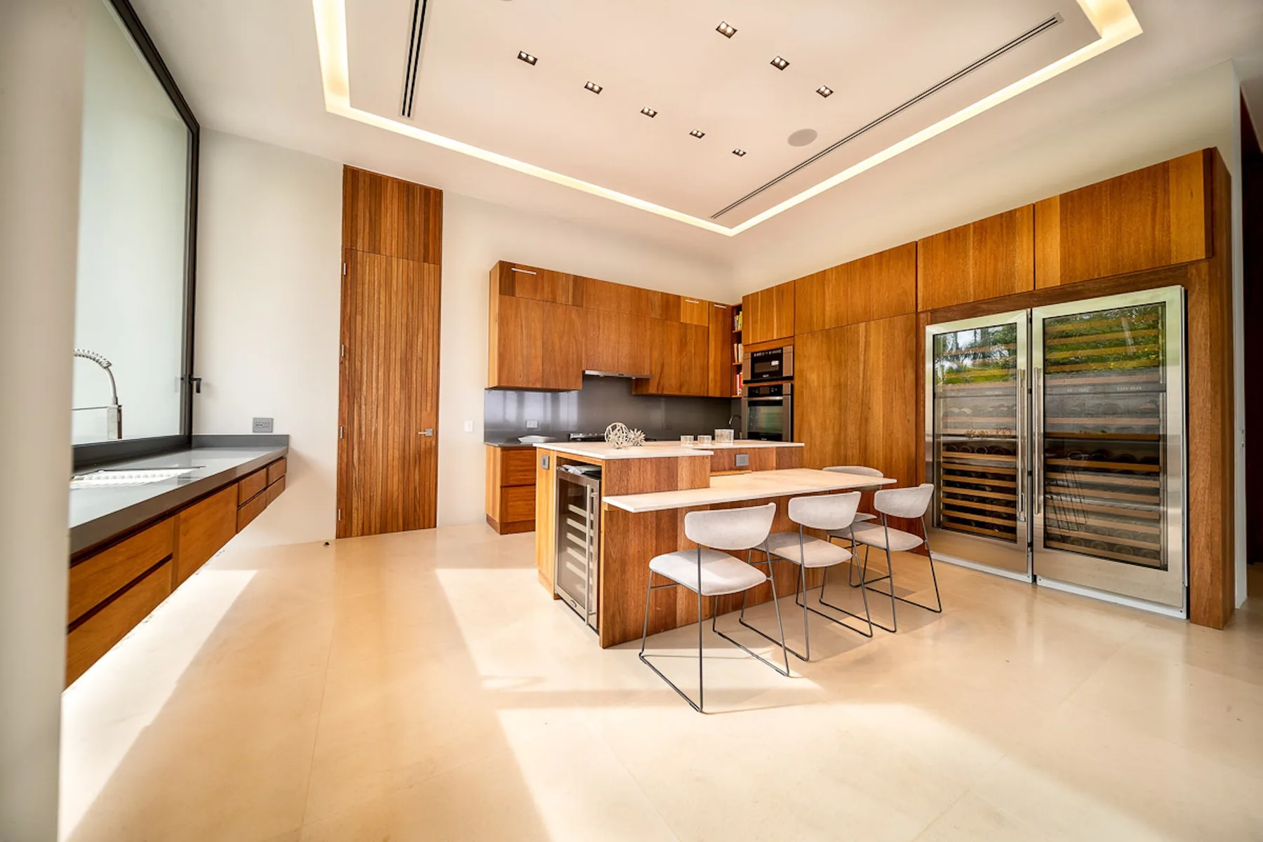 A modern kitchen with a central island, bar seating, and tall wood cabinetry.